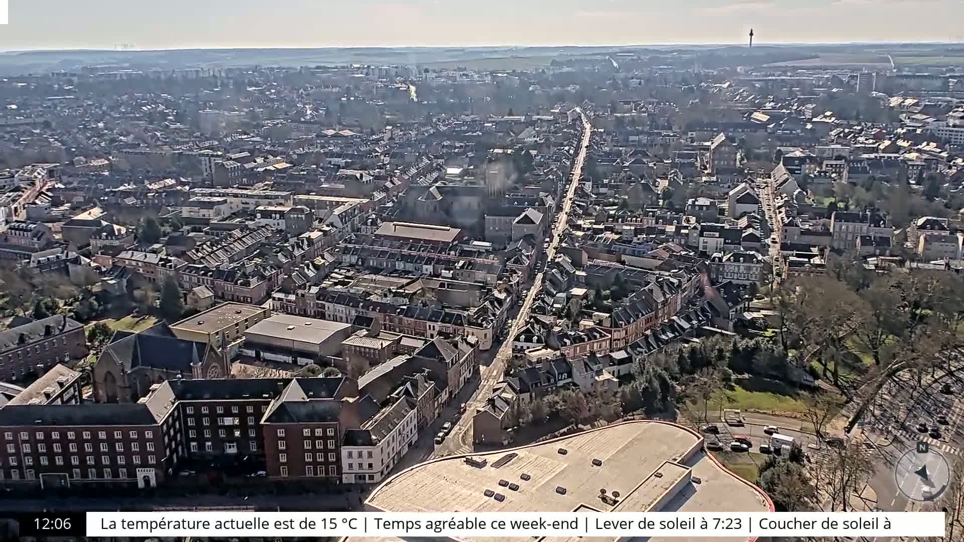 A high-angle, long shot on a sunny day shows a densely packed European city with a long, straight road running through its center.