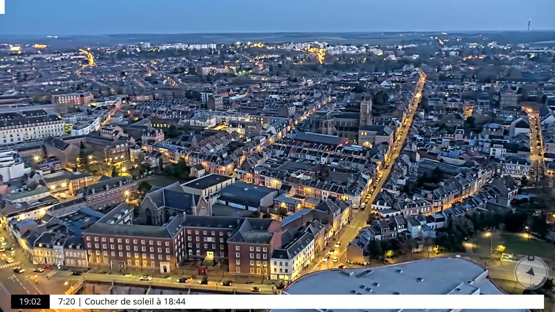 An aerial view at twilight shows a city with illuminated streets and buildings.