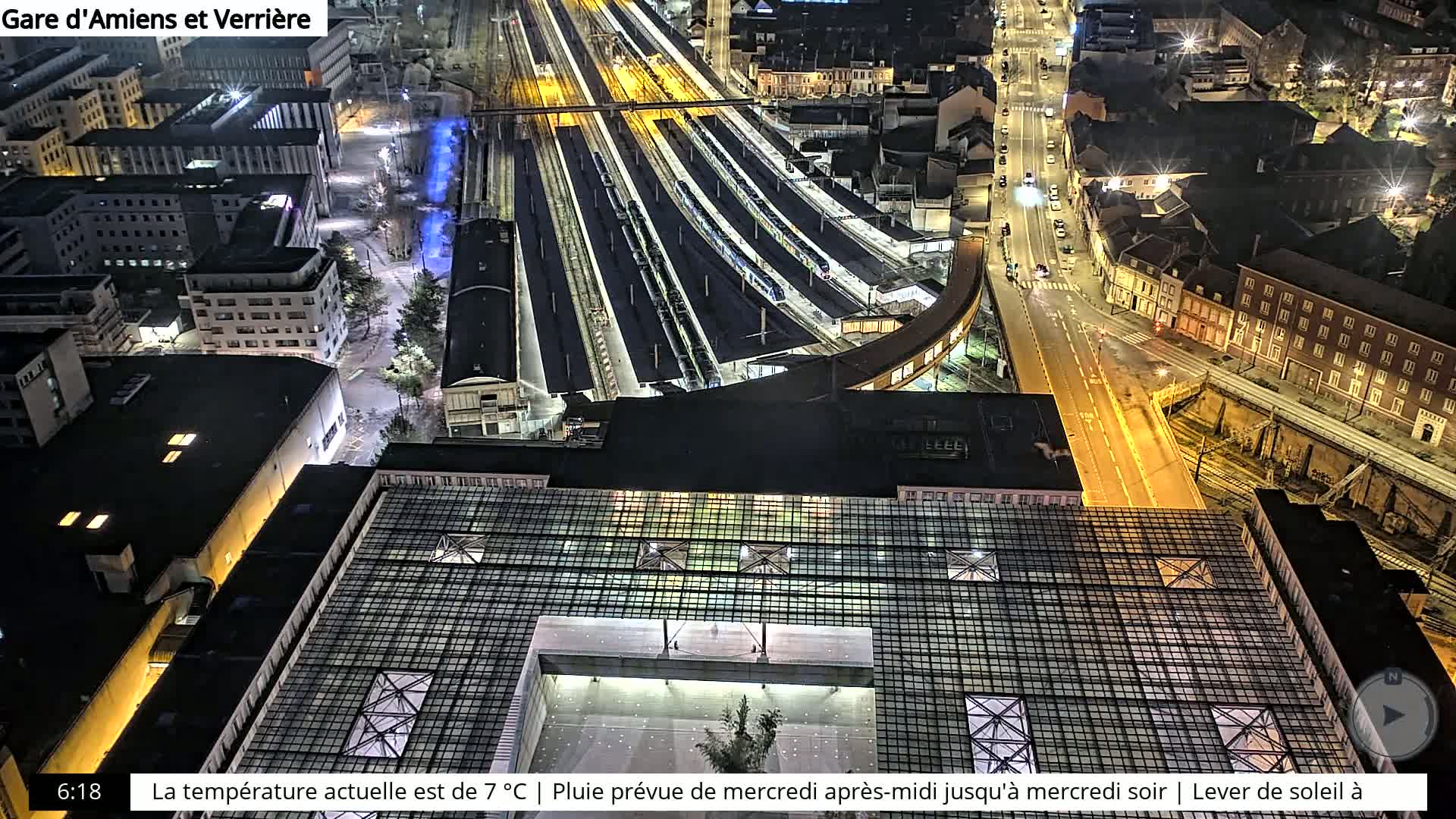 A nighttime aerial view of a train station and surrounding city, illuminated by artificial lights.