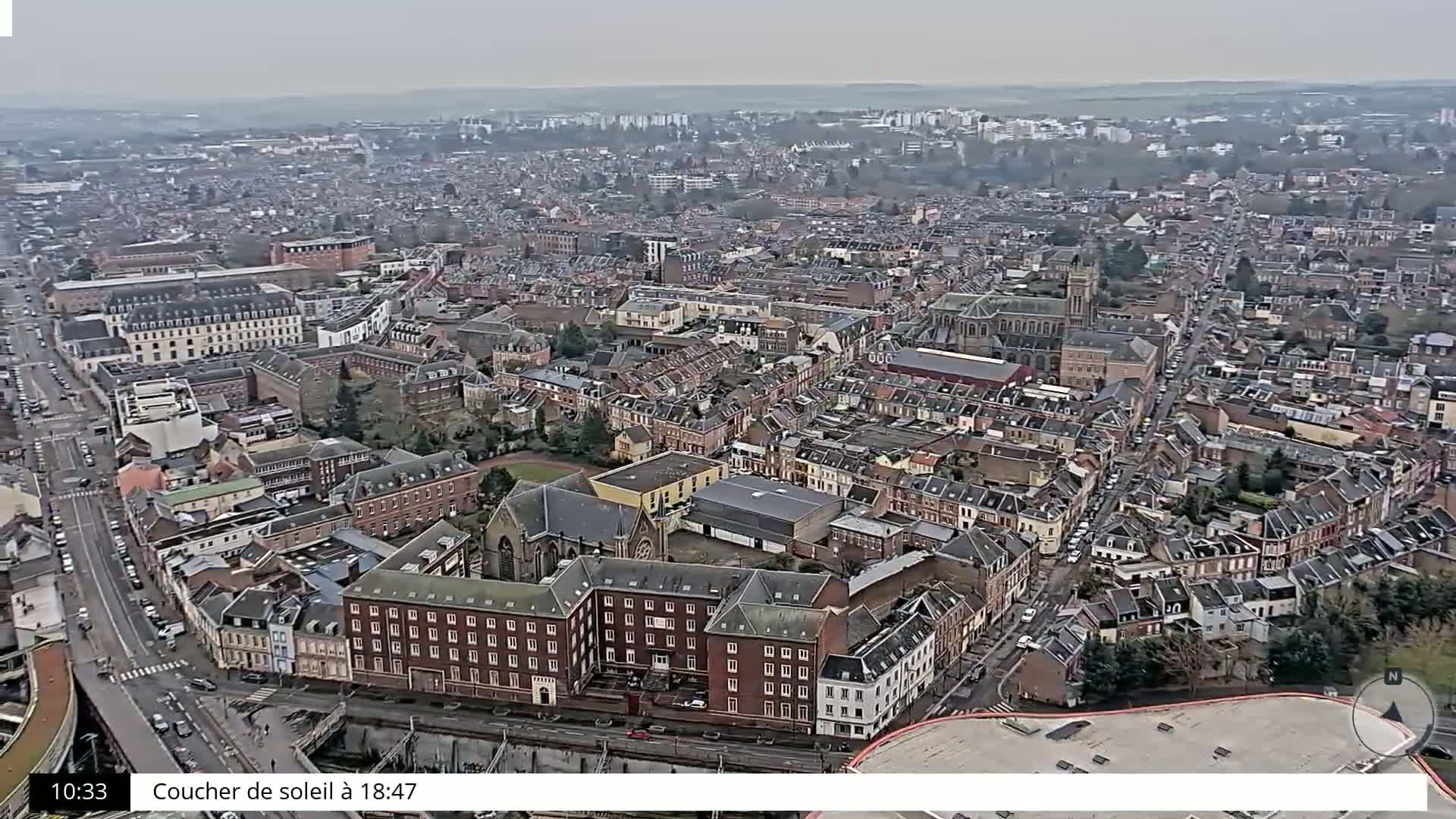 A sprawling city with predominantly brick buildings is viewed from above on an overcast day.