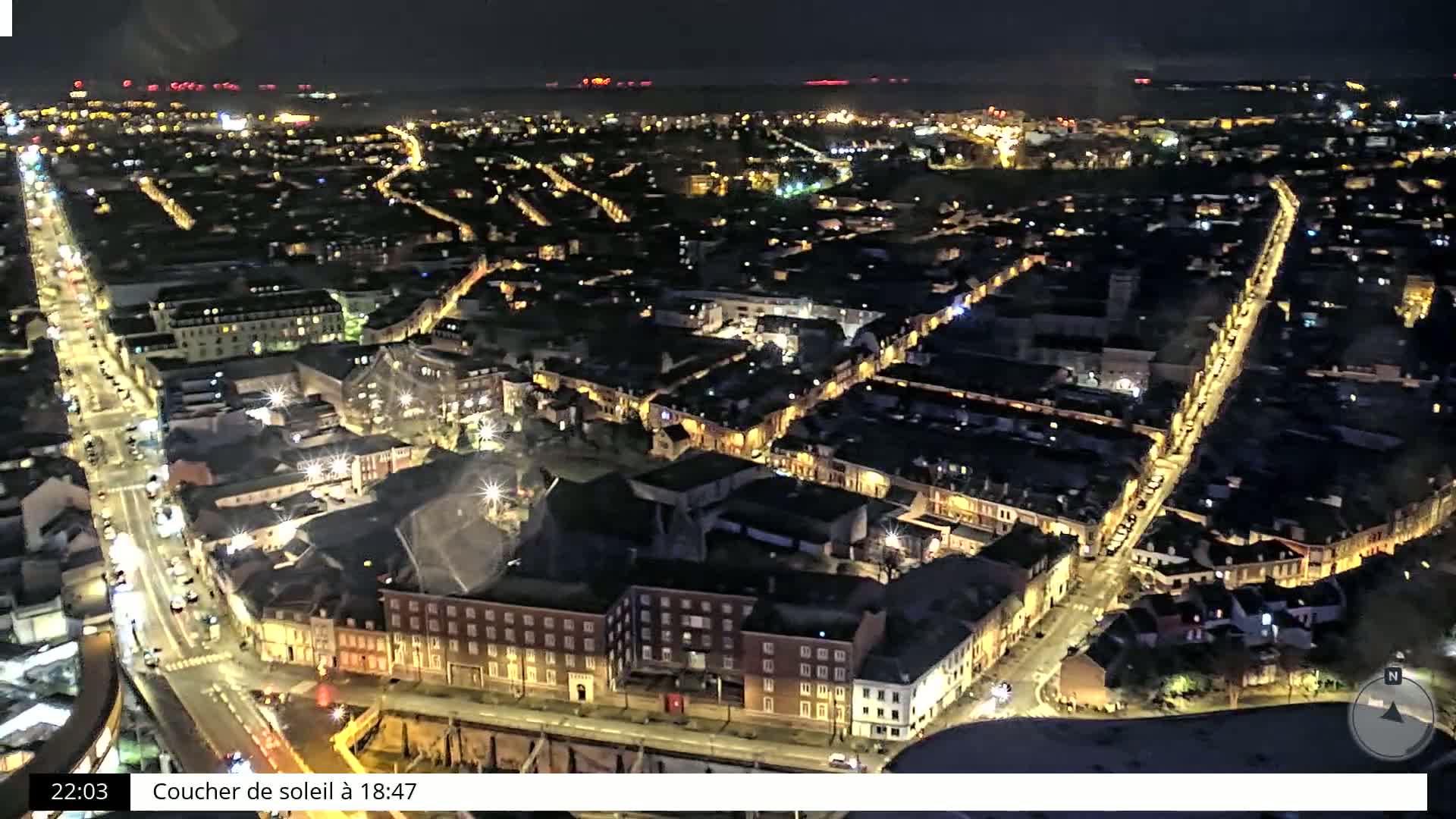 A nighttime aerial view shows a city with illuminated streets and buildings under a dark sky.
