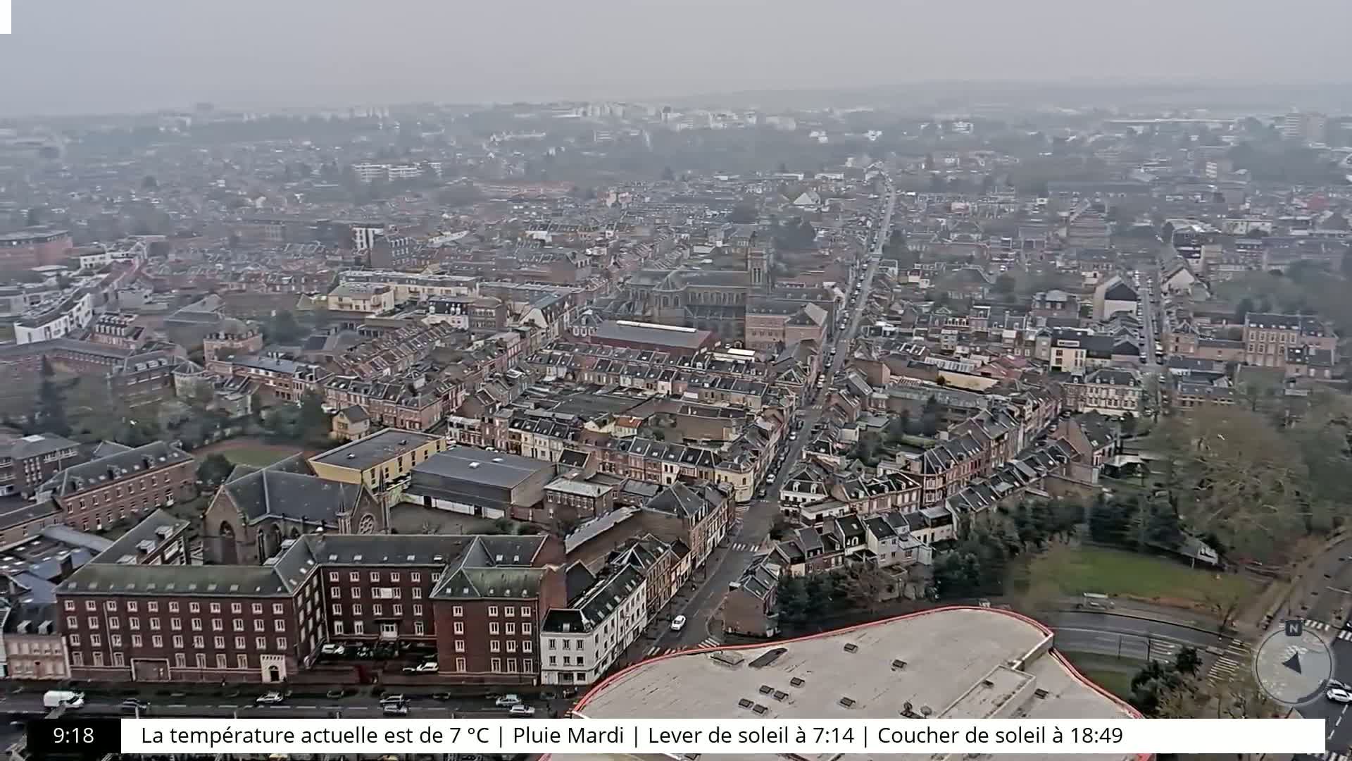A high-angle, long shot of a city on an overcast day shows numerous buildings, streets, and a bit of green space.
