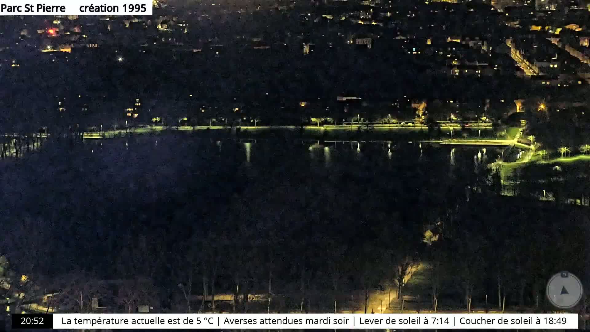 A nighttime aerial view of a park with a body of water, surrounded by dimly lit buildings and trees.
