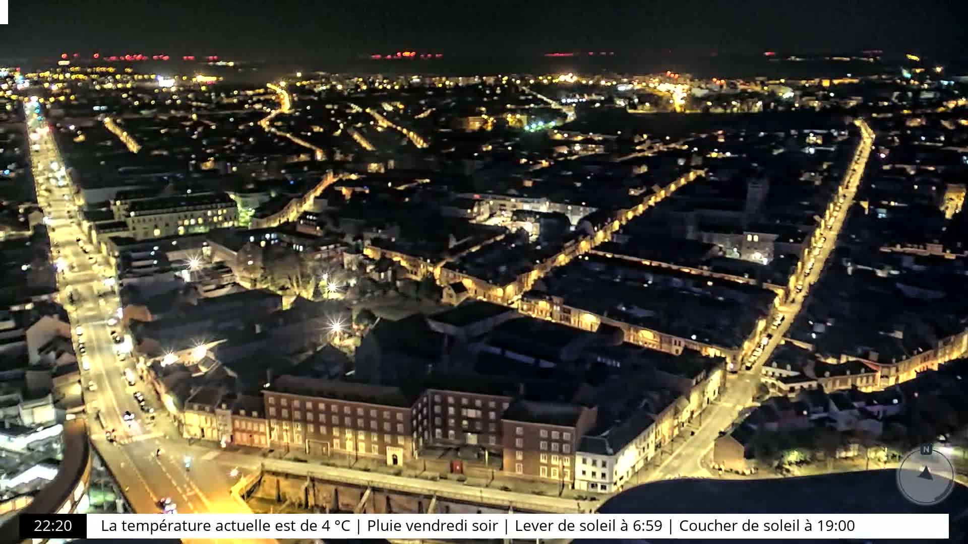 An aerial nighttime view of a city with illuminated streets and buildings under rainy conditions.