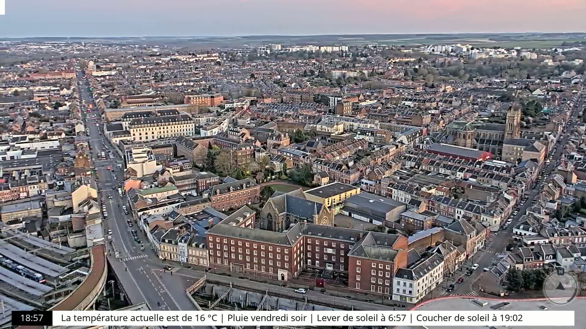 An aerial view shows a densely populated city with many brick buildings under an overcast sky, possibly at dusk or dawn.