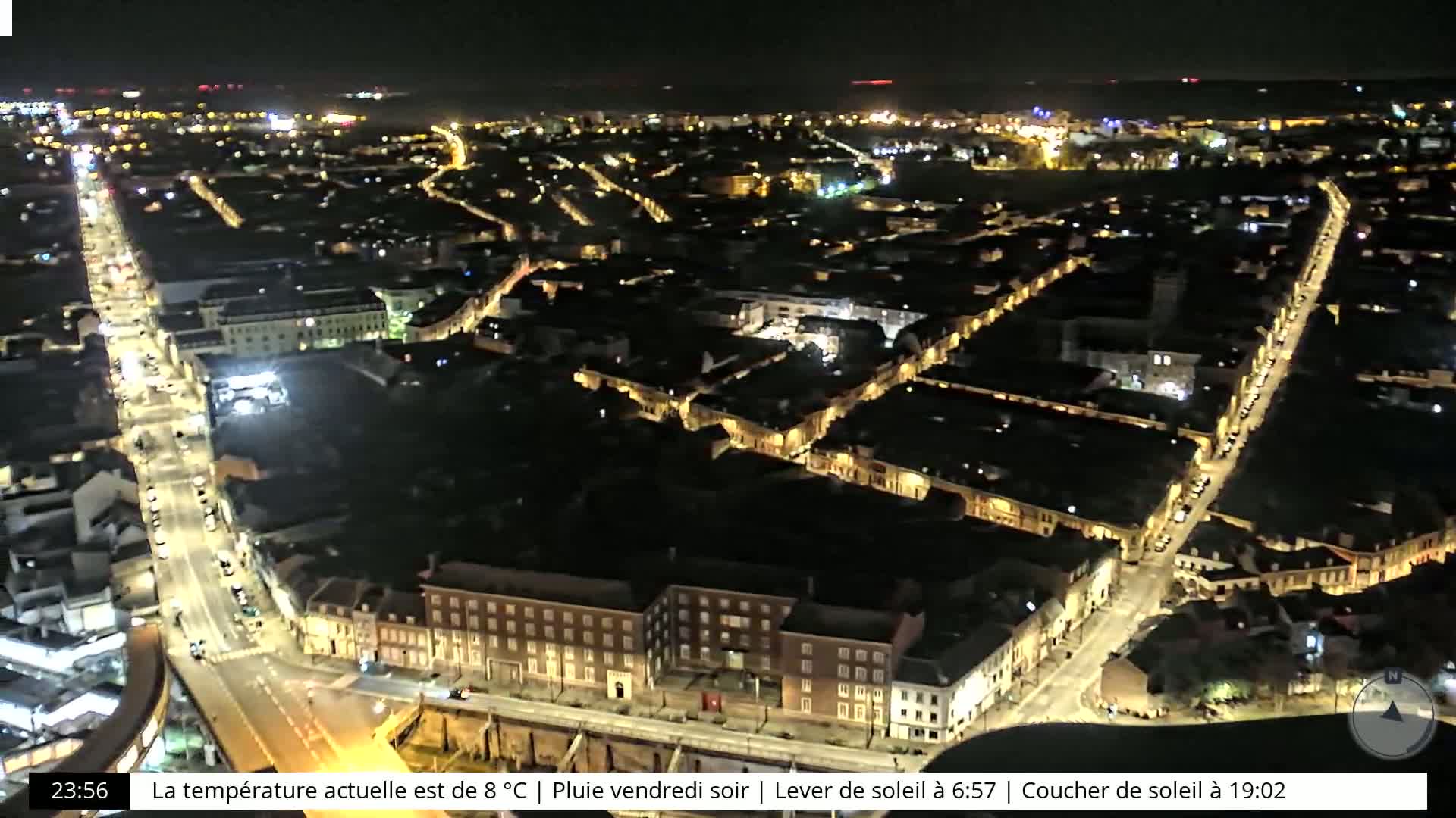 A nighttime aerial view of a city with illuminated streets and buildings under rainy conditions.