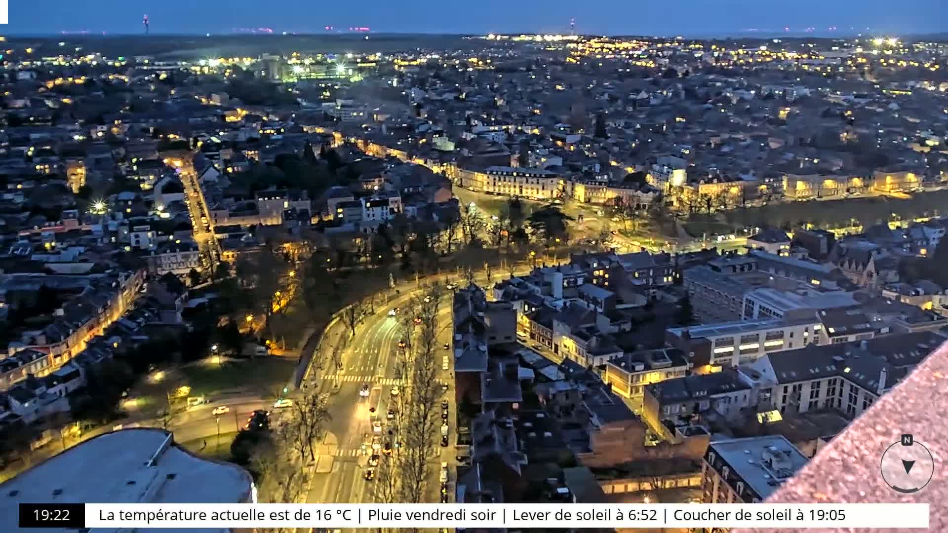 A nighttime aerial view of a city with illuminated streets and buildings under a partly cloudy sky.