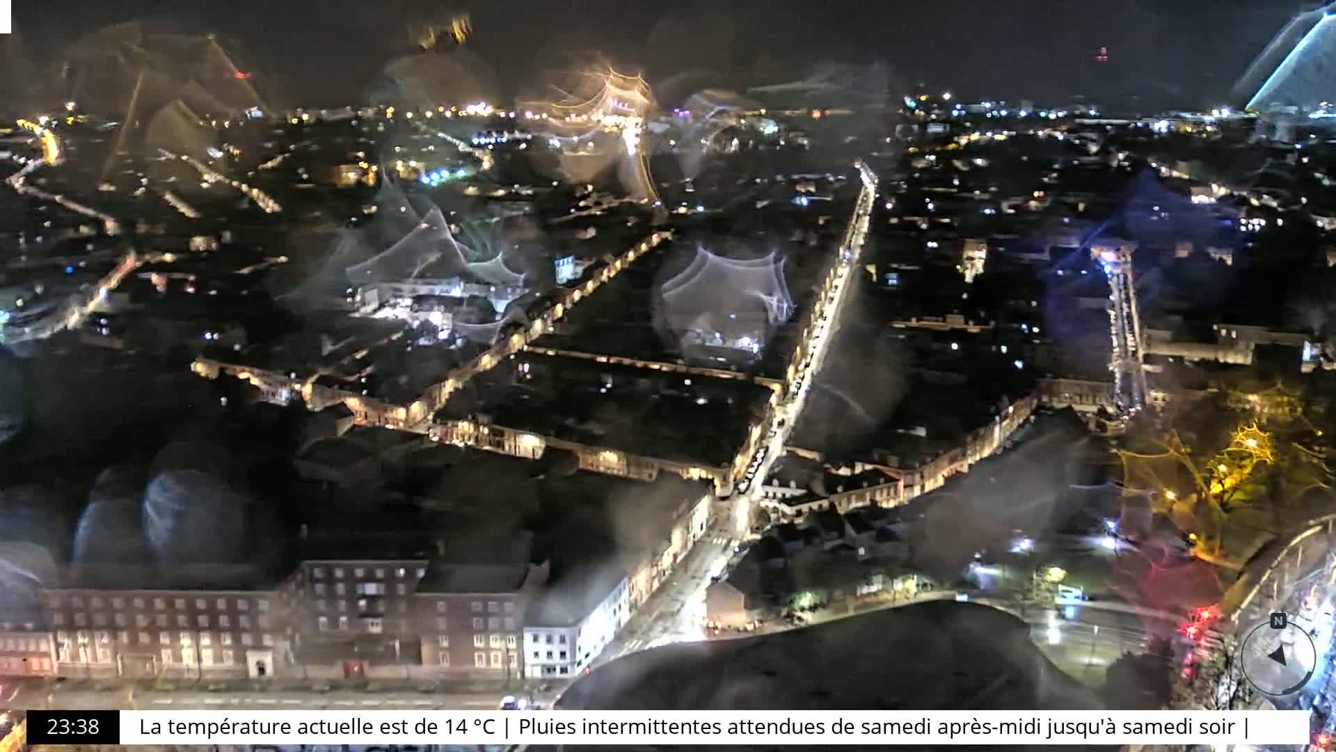 A nighttime aerial view of a city street with intermittent rain and city lights visible through a rain-streaked window.