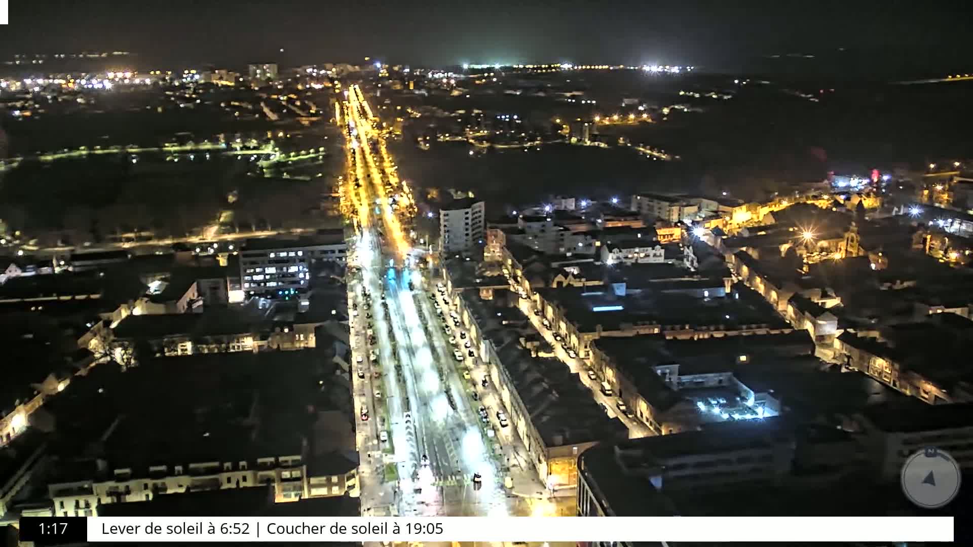 A nighttime aerial view shows a city with brightly lit streets and buildings, under clear skies.