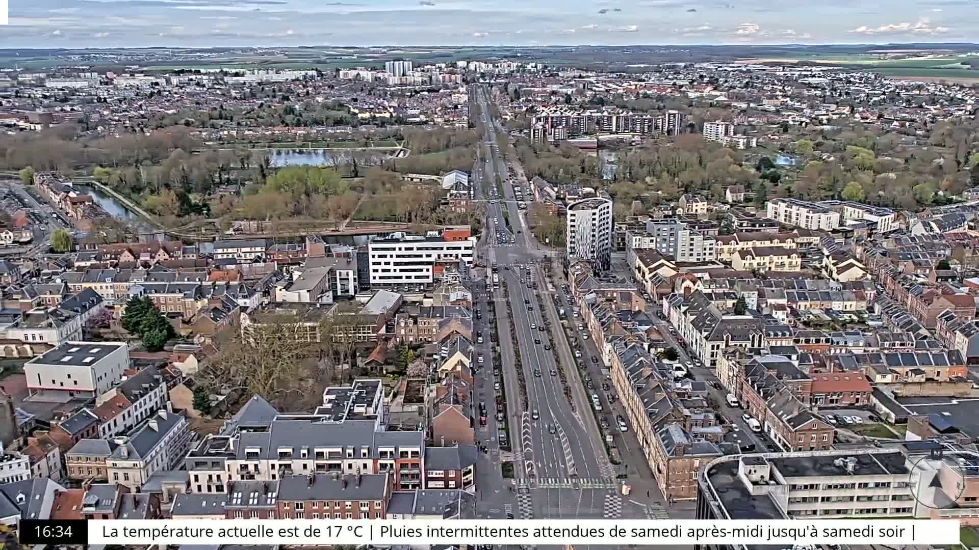 An aerial view of a city with a long road running through it, under a partly cloudy sky.