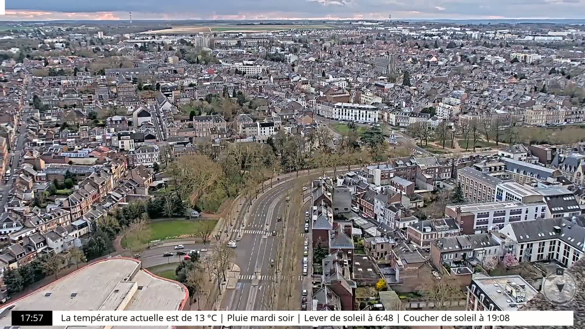 A high-angle view of a city with a main road running through it under an overcast sky, with rain falling.