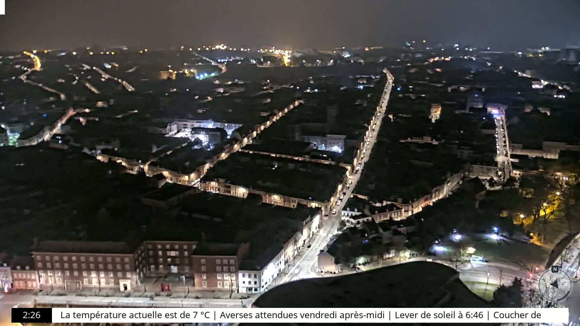 A nighttime aerial view of a city with illuminated streets and buildings under a dark, possibly overcast sky.