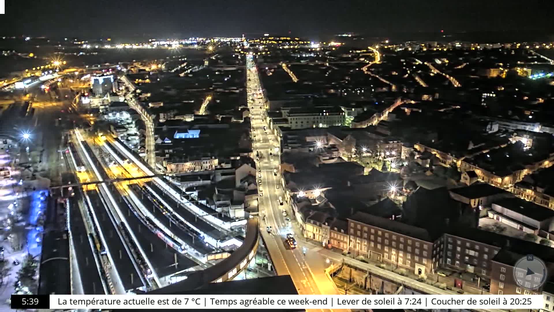 A nighttime aerial view of a city with a train station and brightly lit streets and buildings.