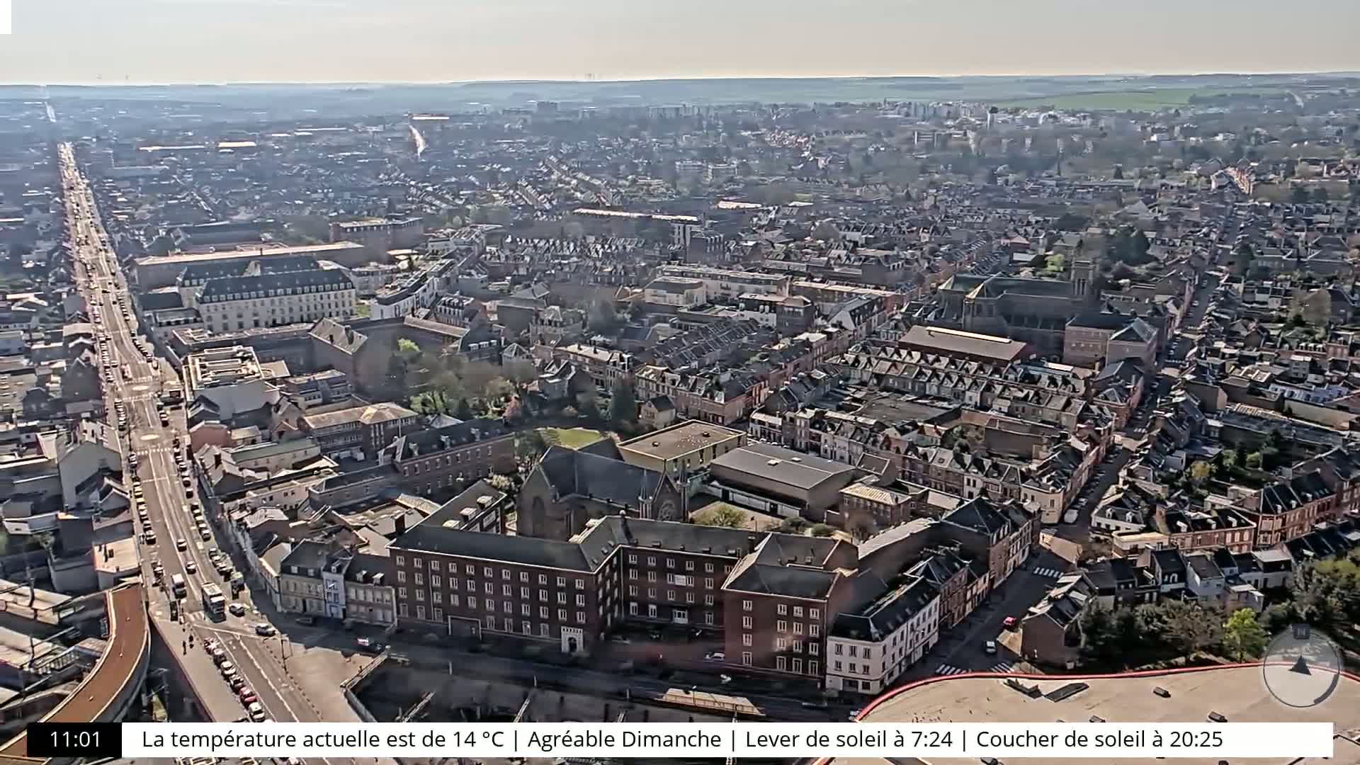 A high-angle, sunny view of a dense city with many brick buildings and a long road running through it.