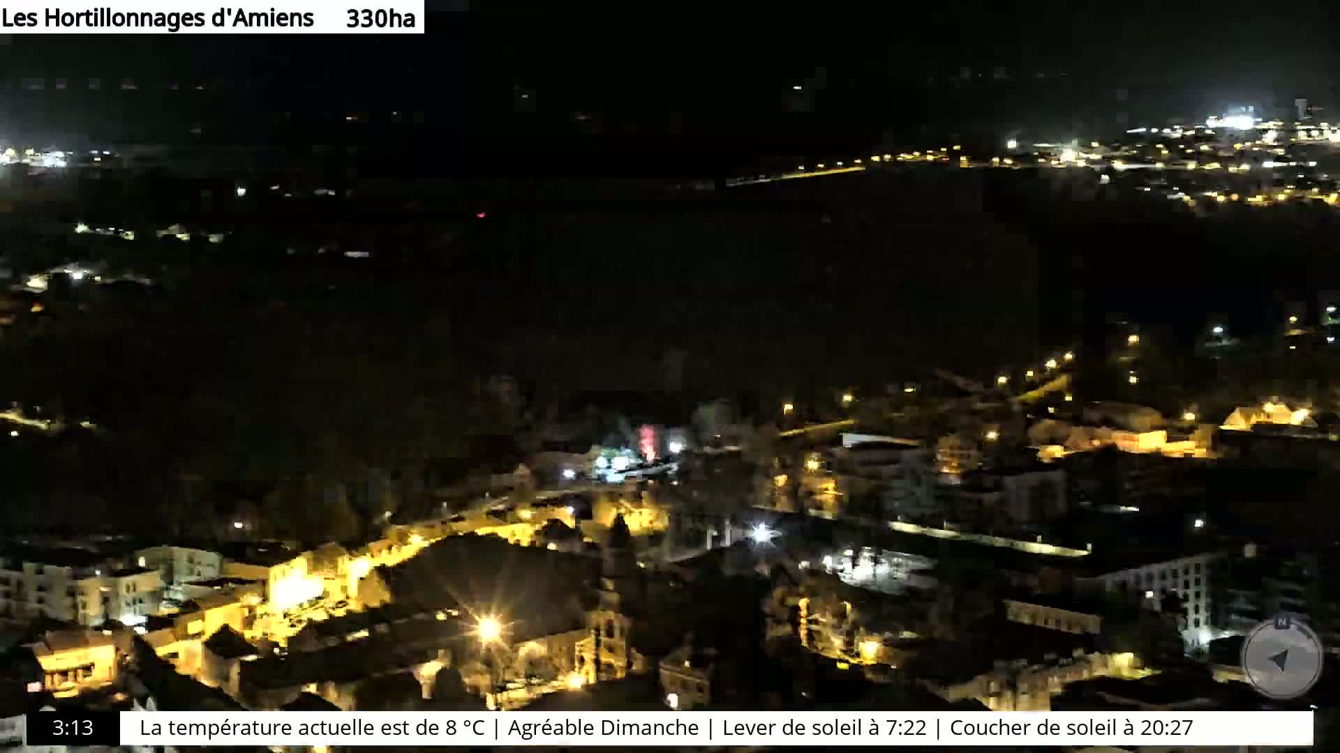 A nighttime aerial view of a town with scattered lights, overlooking a dark body of water.