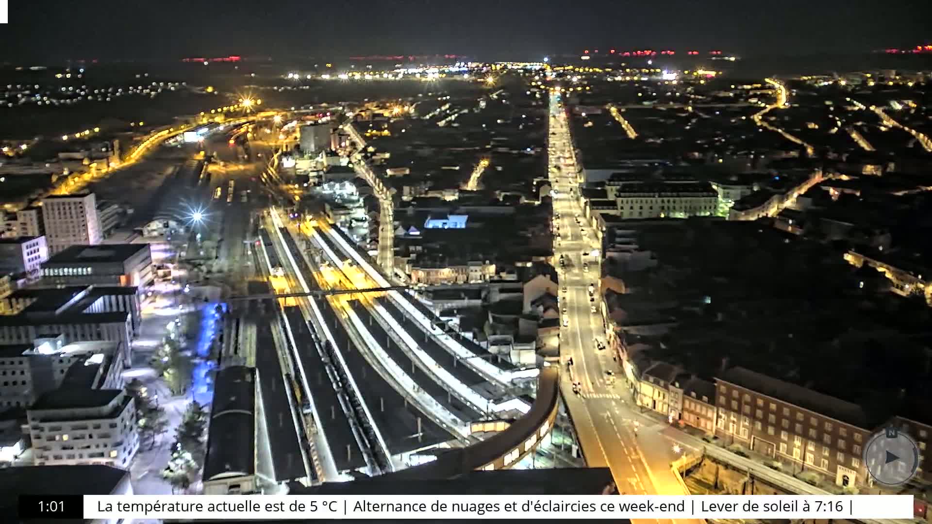 An aerial nighttime view of a city with a train station and brightly lit streets.