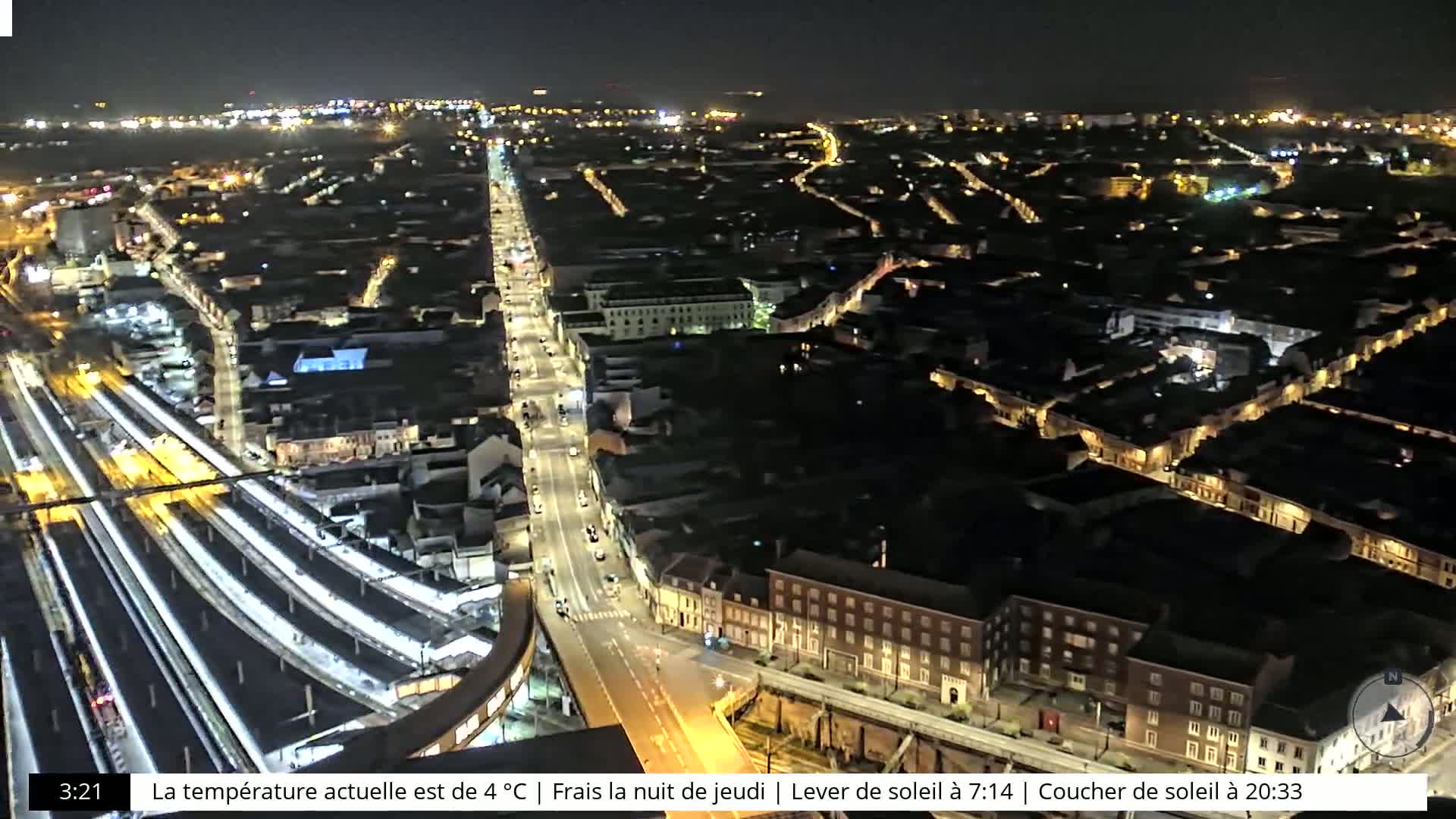 A nighttime aerial view of a city with a train station and illuminated streets and buildings.