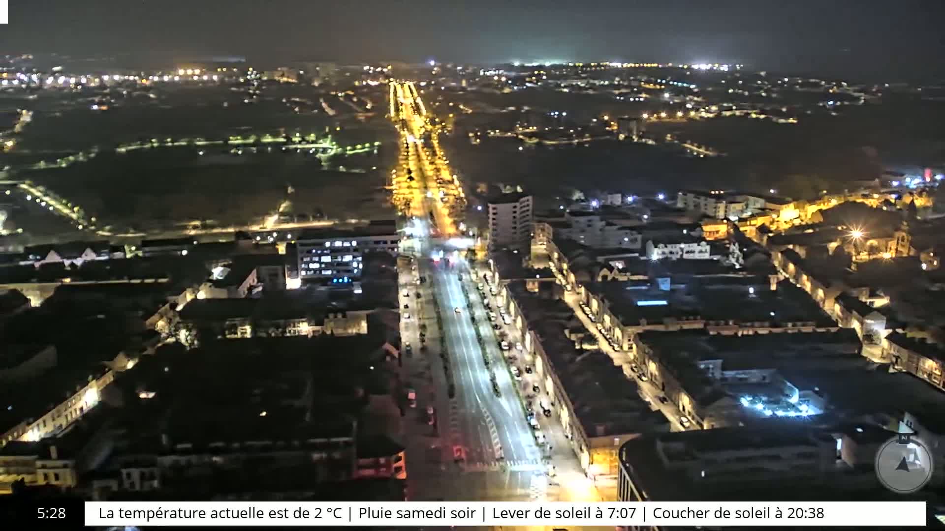 An aerial nighttime view of a city with rain, showing brightly lit streets and buildings.