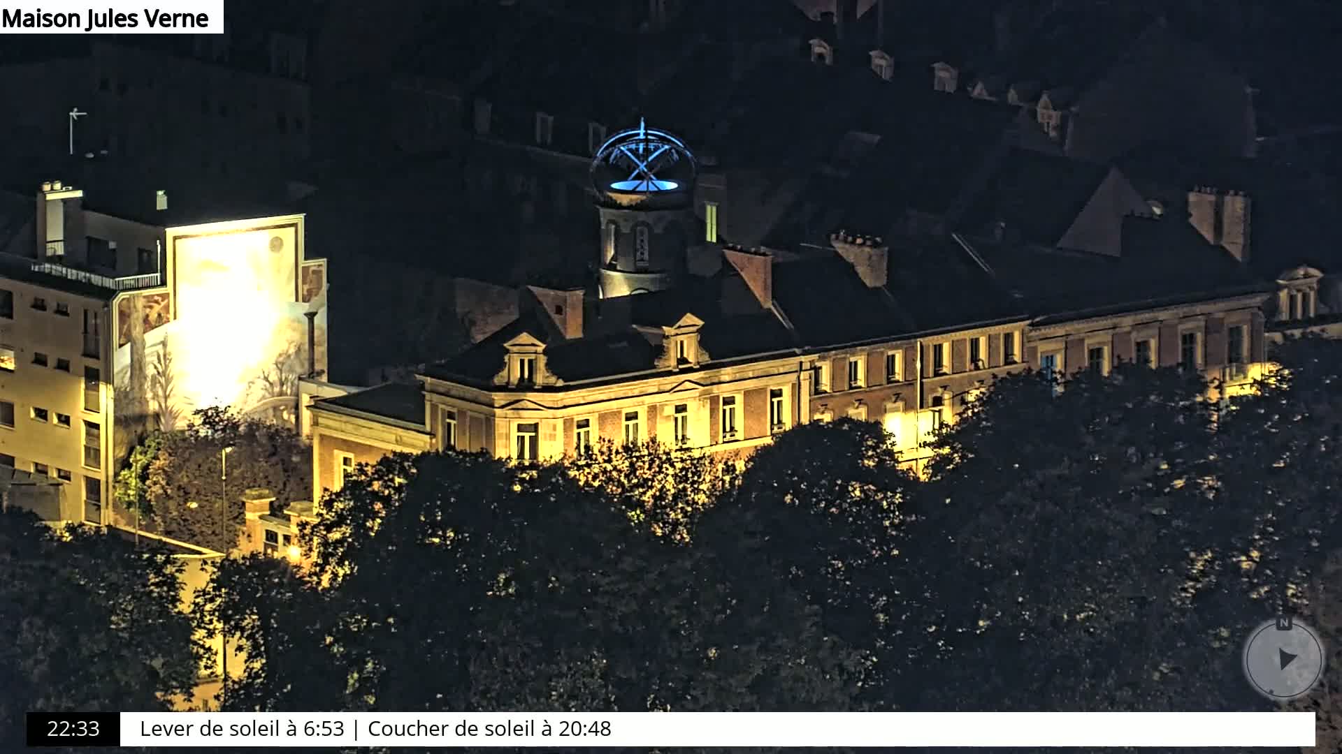 A large building with a distinctive cupola, illuminated at night, is partially obscured by trees.