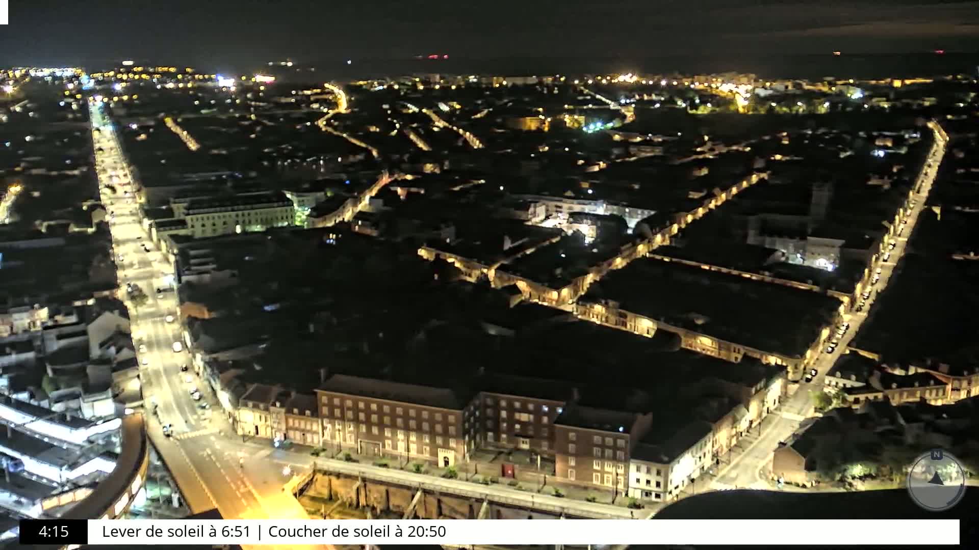 A nighttime aerial view shows a city with illuminated streets and buildings under a clear sky.