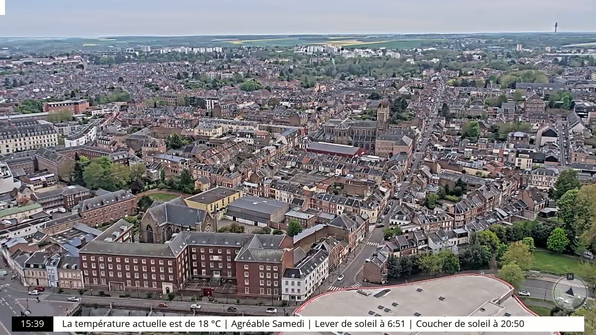 A sprawling city landscape is visible on a partly sunny day, with numerous buildings and green spaces.