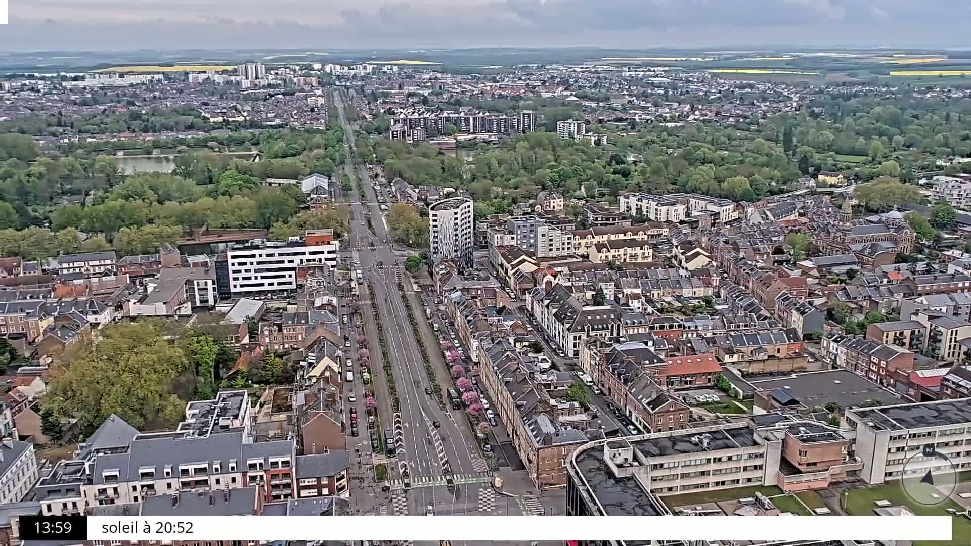 An aerial view shows a city with many houses and trees under an overcast sky.