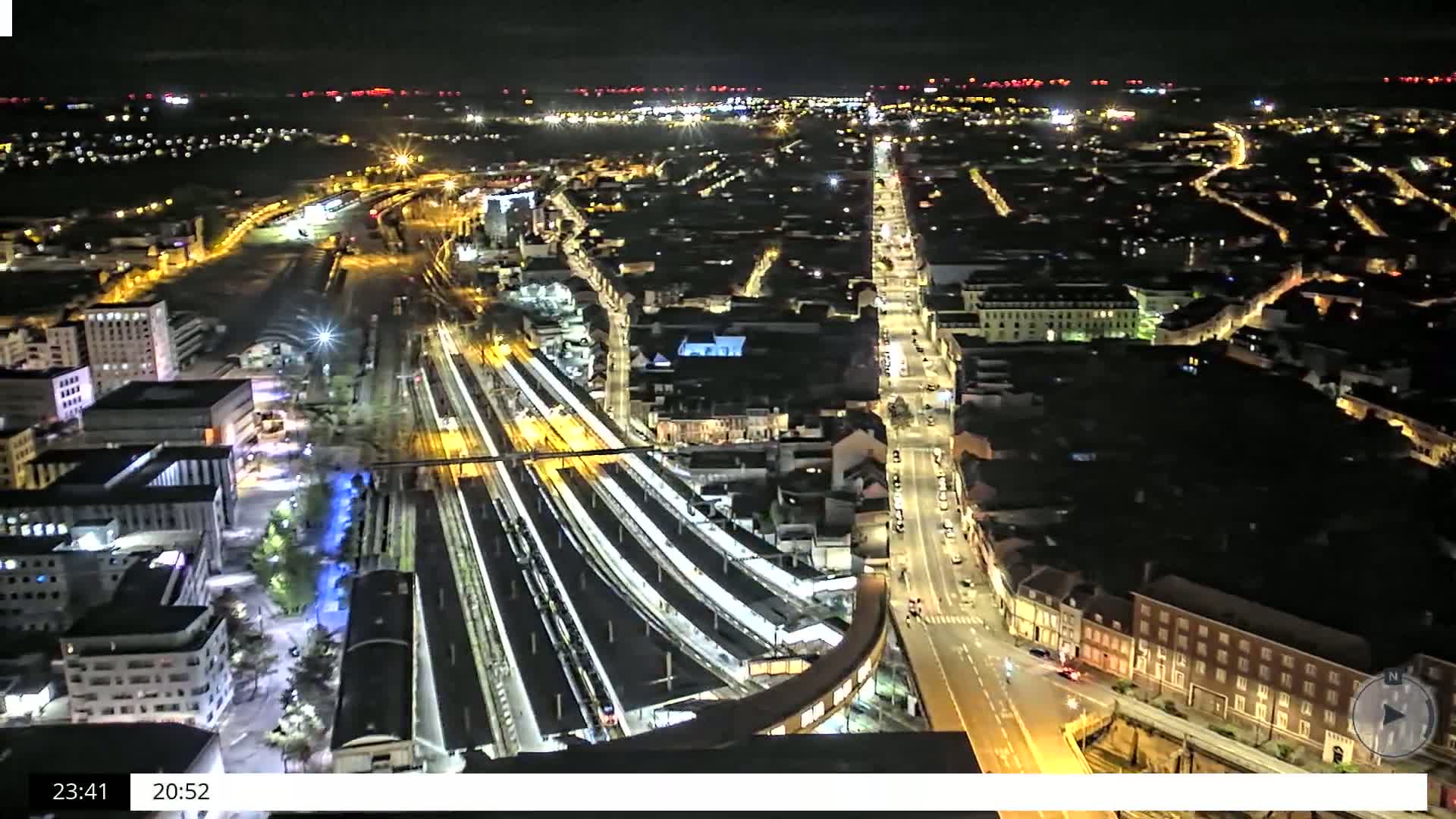 A nighttime aerial view of a city's illuminated train station and surrounding streets.