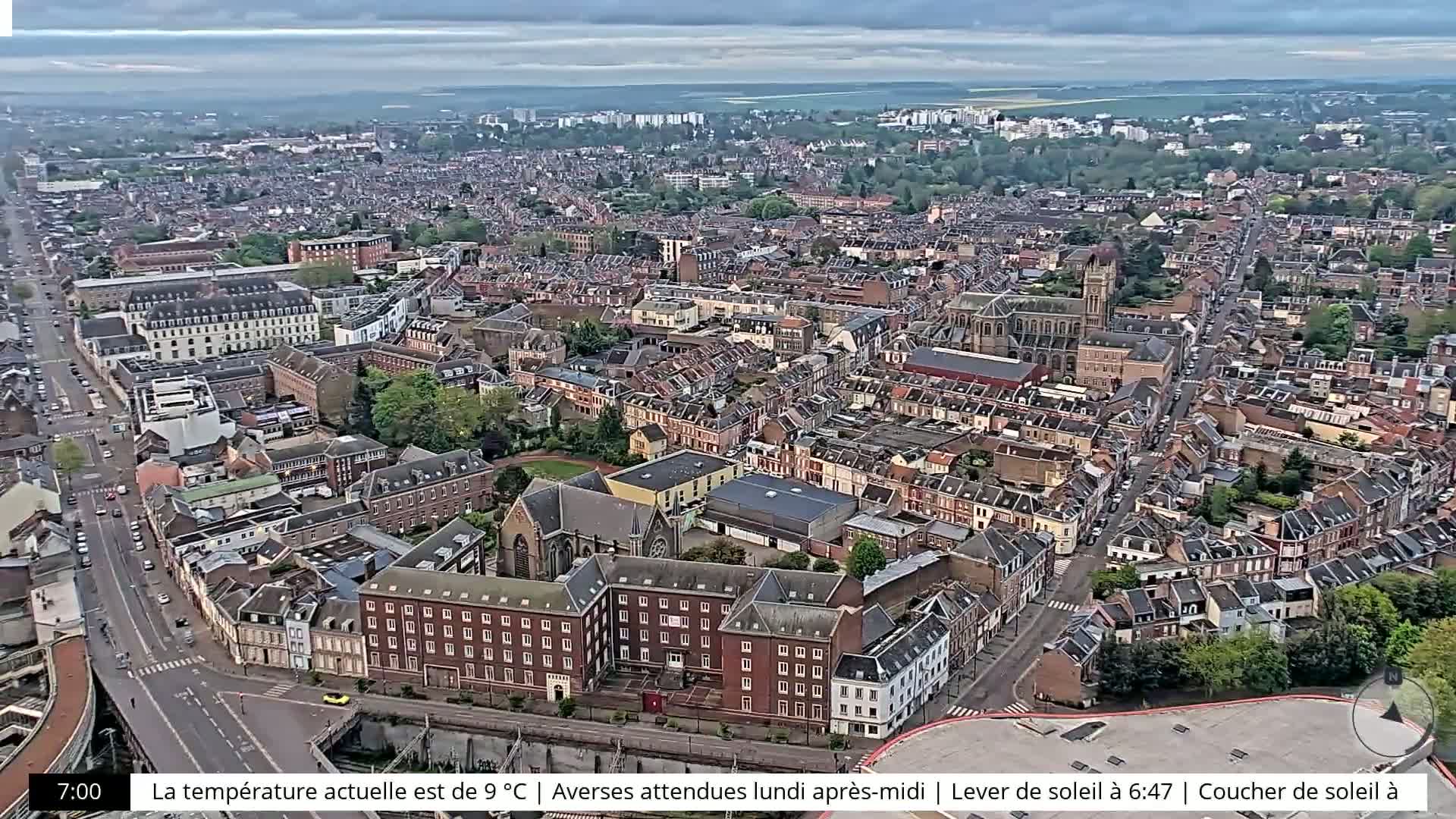 An aerial view of a dense city under an overcast sky shows many brick buildings, streets, and trees.
