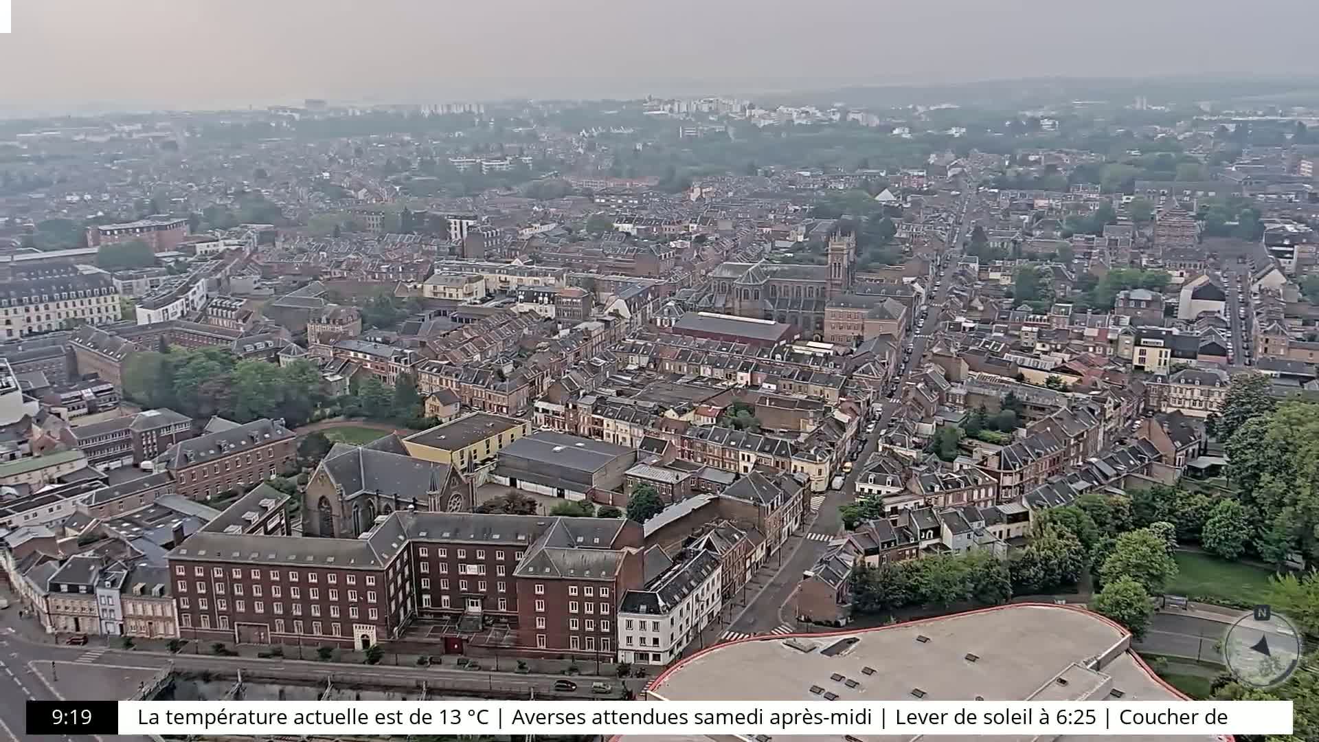 A hazy aerial view shows a densely populated city with many brick buildings and green spaces.