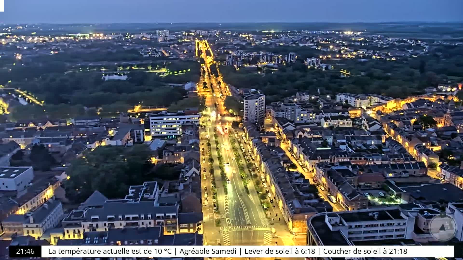 A nighttime aerial view shows a city with brightly lit streets and buildings, surrounded by dark green areas.