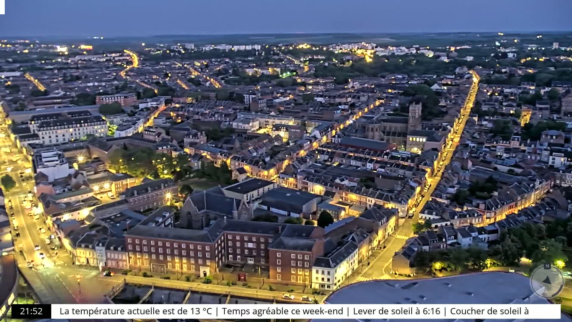An aerial view at twilight shows a city illuminated by streetlights, with many buildings and streets visible.