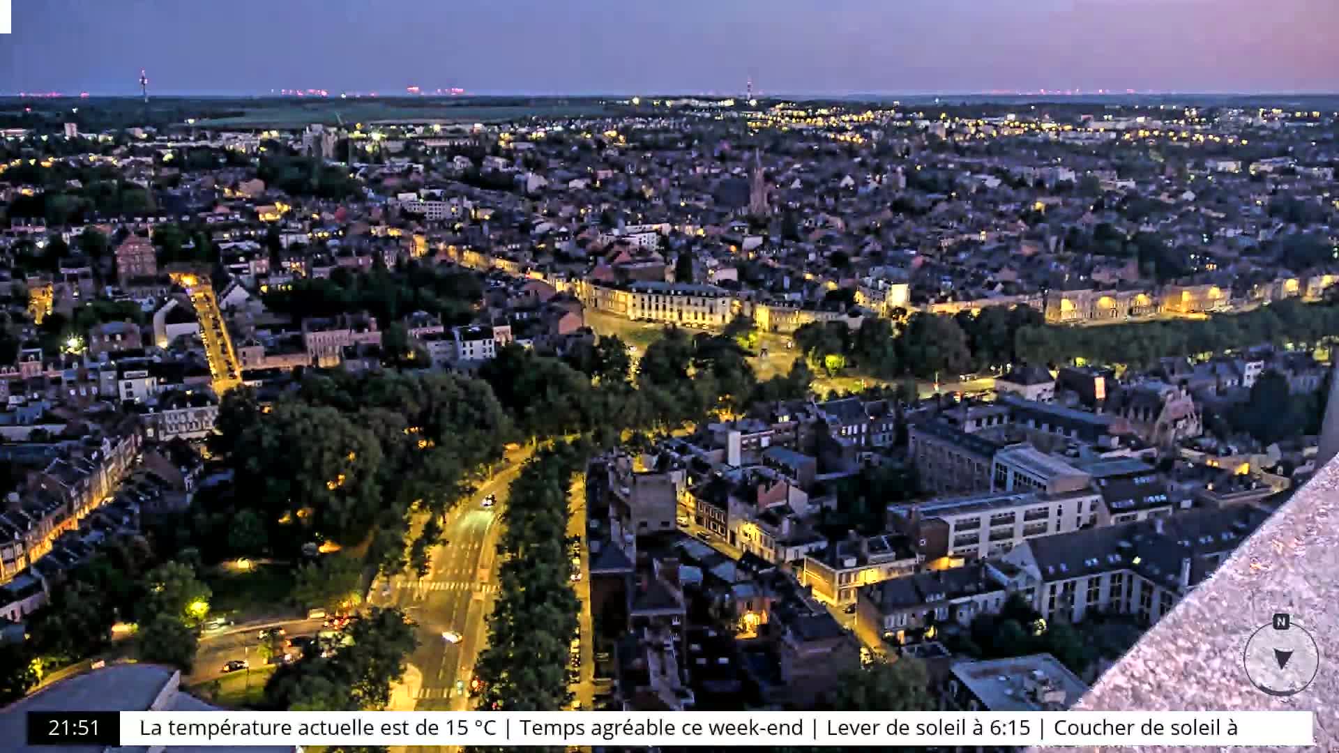 An aerial nighttime view of a city illuminated by streetlights, under a twilight sky.