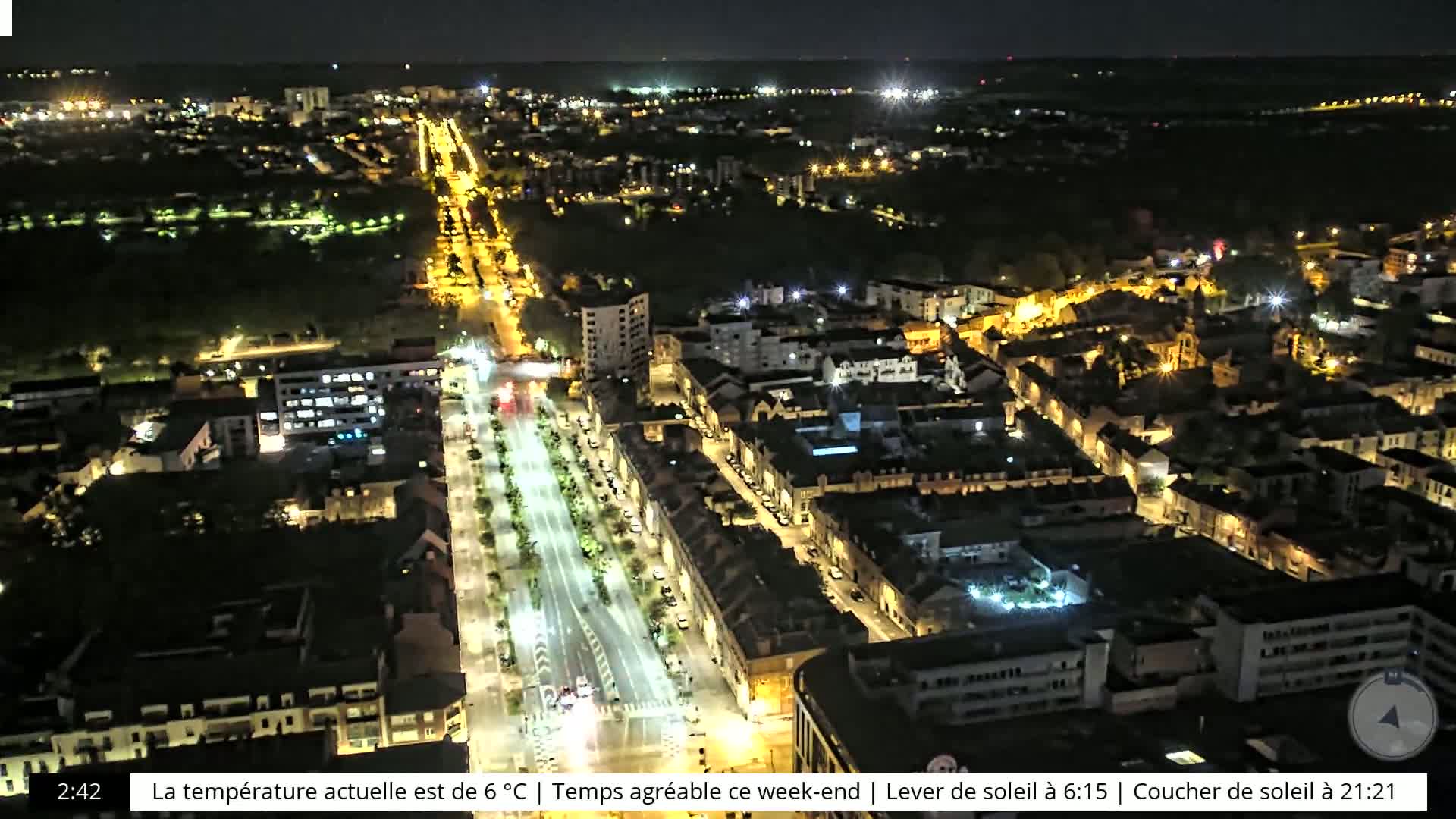 A nighttime aerial view of a city with brightly lit streets and buildings, surrounded by darker, tree-covered areas.