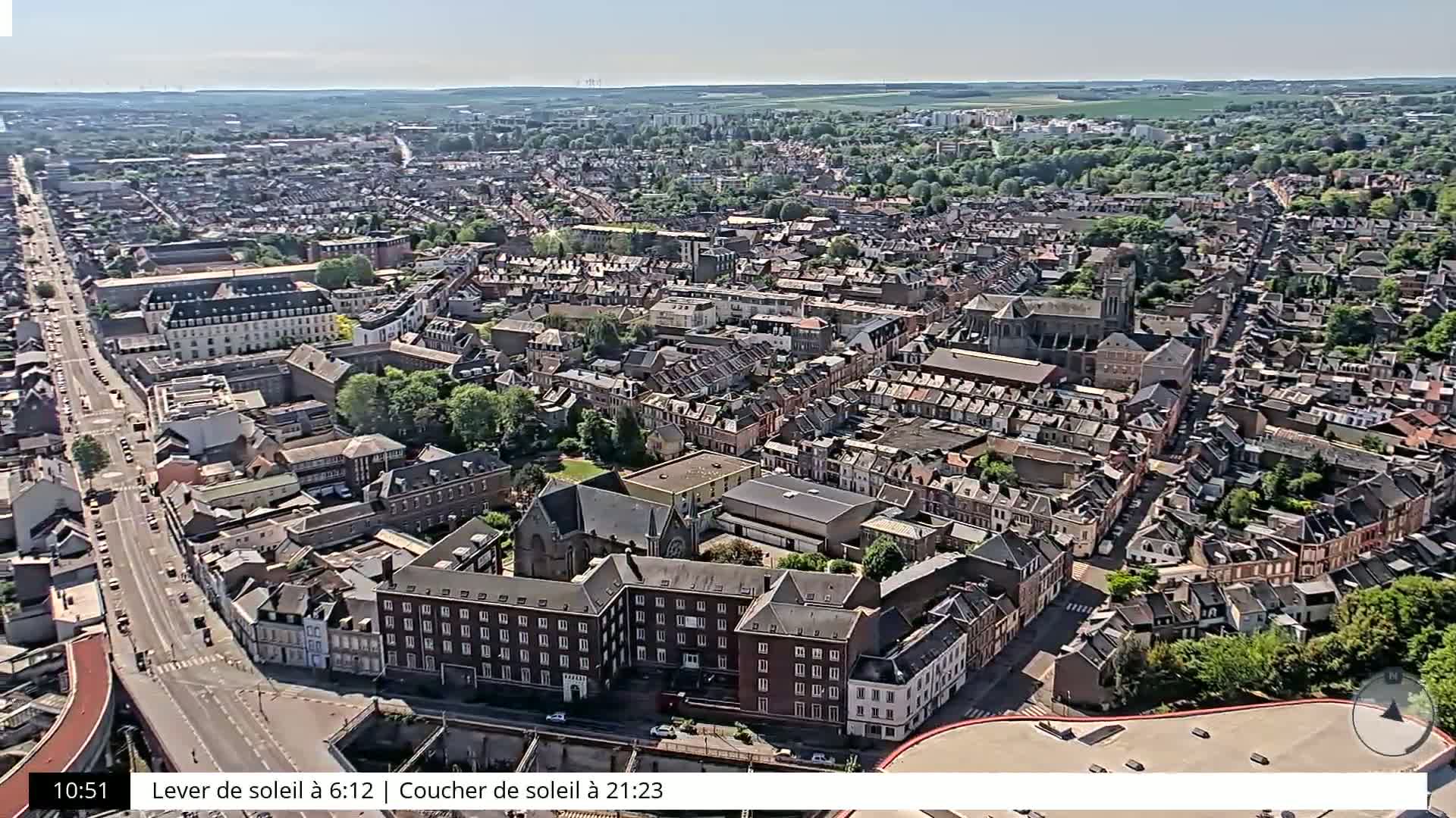 A high-angle, long shot of a densely packed European town on a sunny day, showing numerous buildings and streets, with a large road cutting through the center.