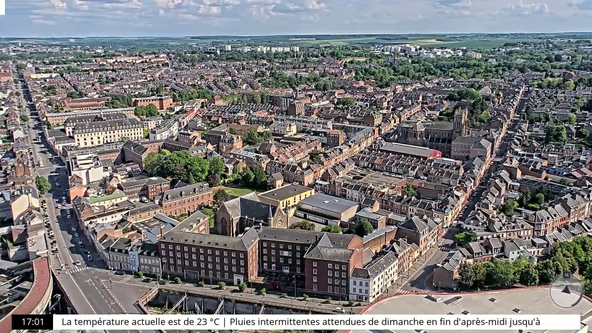 An aerial view shows a densely populated city under partly cloudy skies.