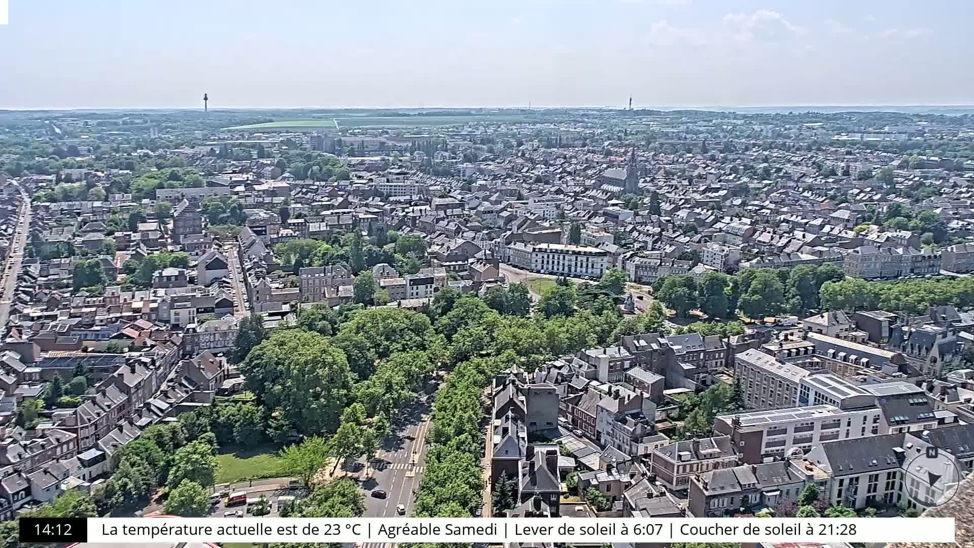 A high-angle, sunny view of a dense city with many buildings and green spaces.