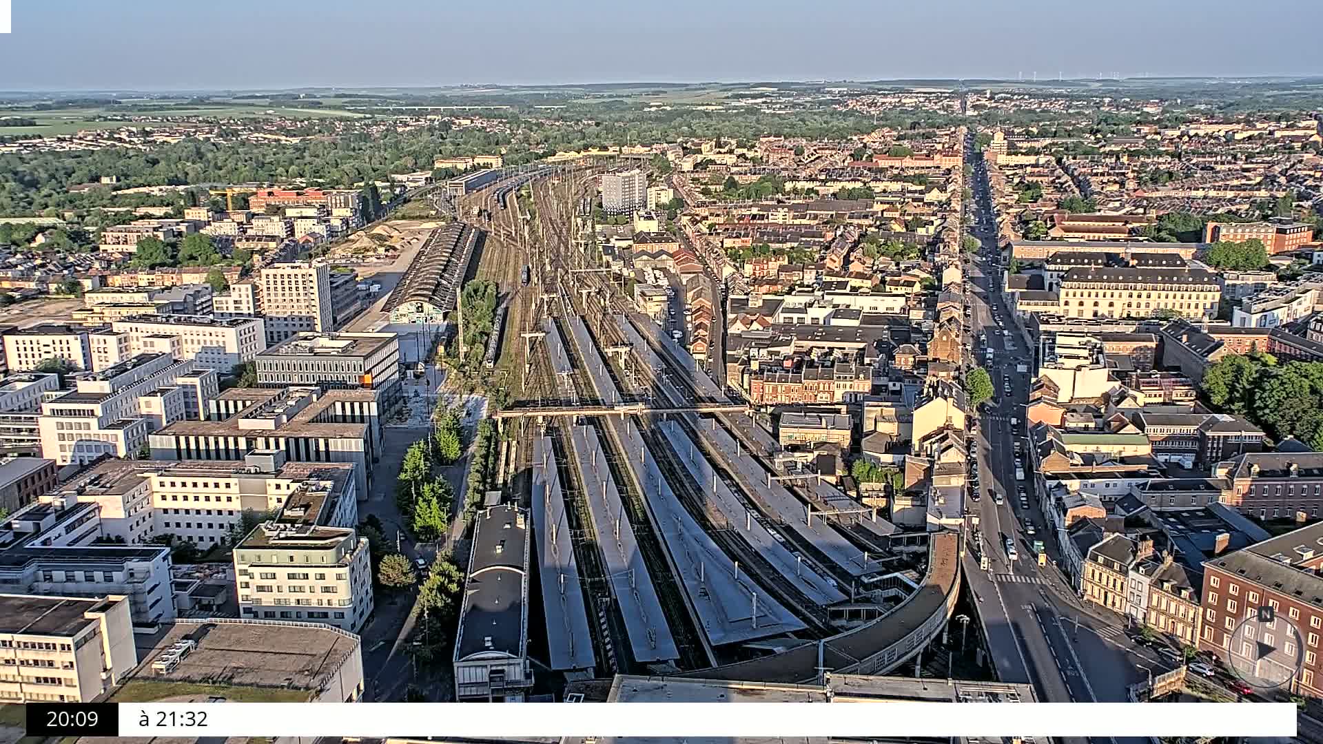 An aerial view of a city on a partly sunny day, showing a large train station and surrounding residential areas.