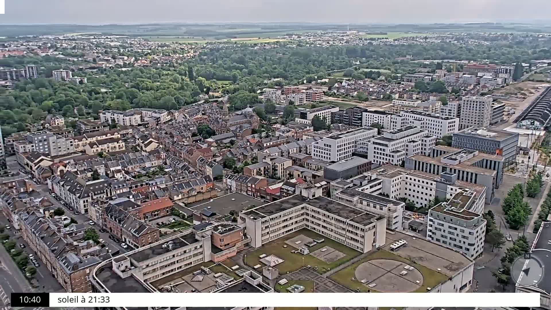 An aerial view shows a densely populated area with many residential buildings and some larger structures, under an overcast sky.