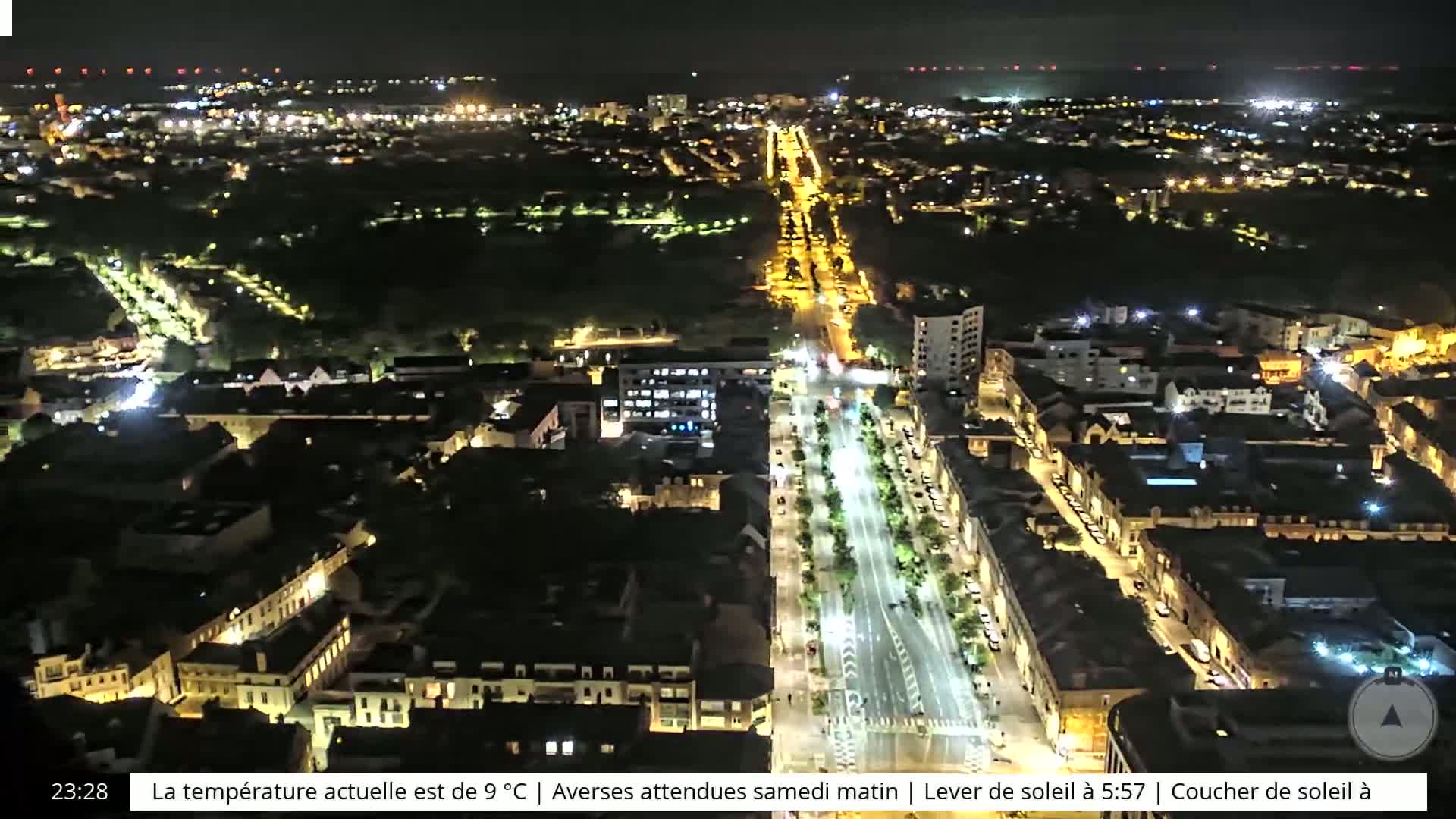 A nighttime aerial view of a city with brightly lit streets and buildings, showing a large park-like area in the center.