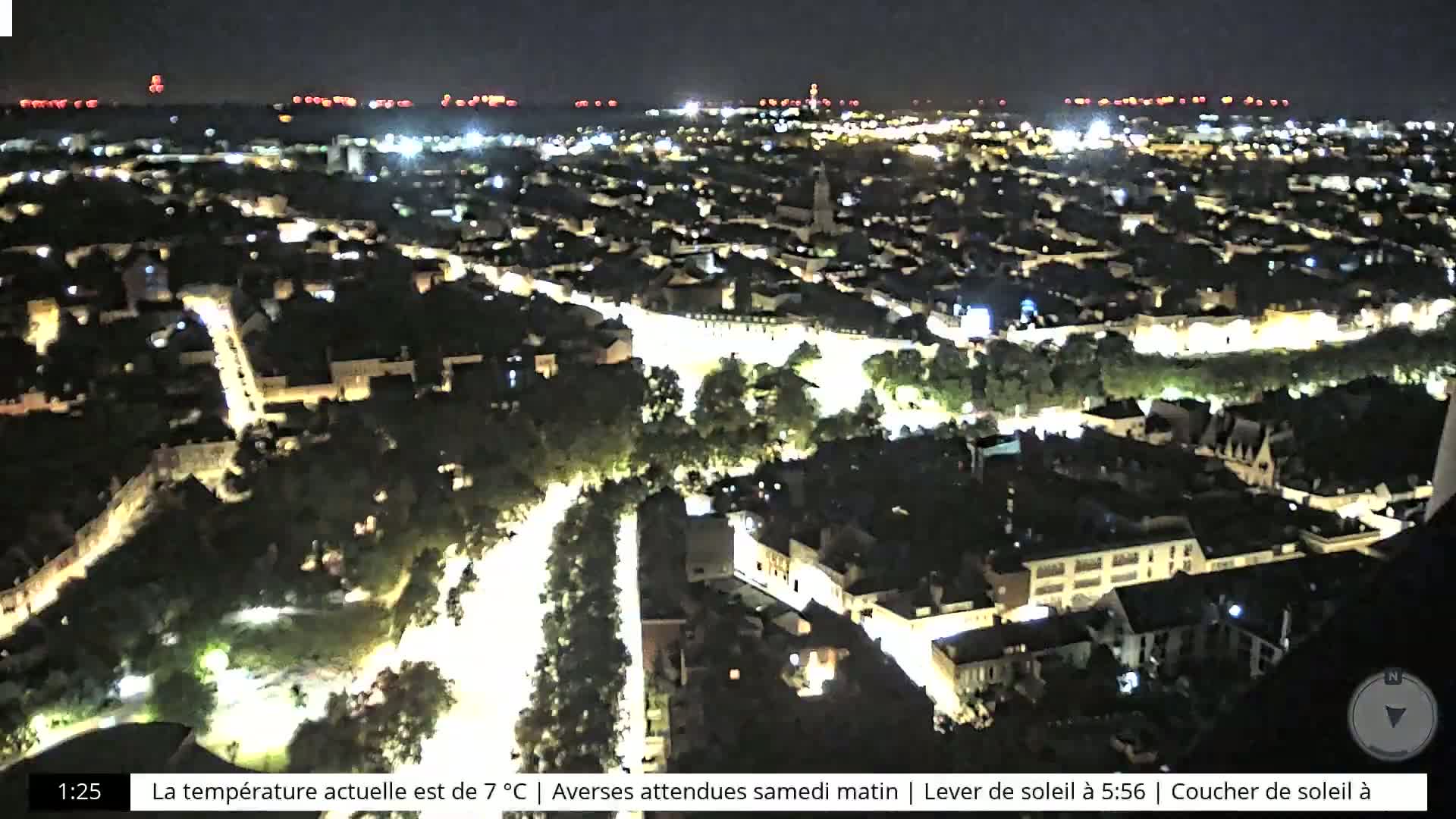 A nighttime aerial view of a city illuminated by streetlights, with a distant shoreline faintly visible in the background.