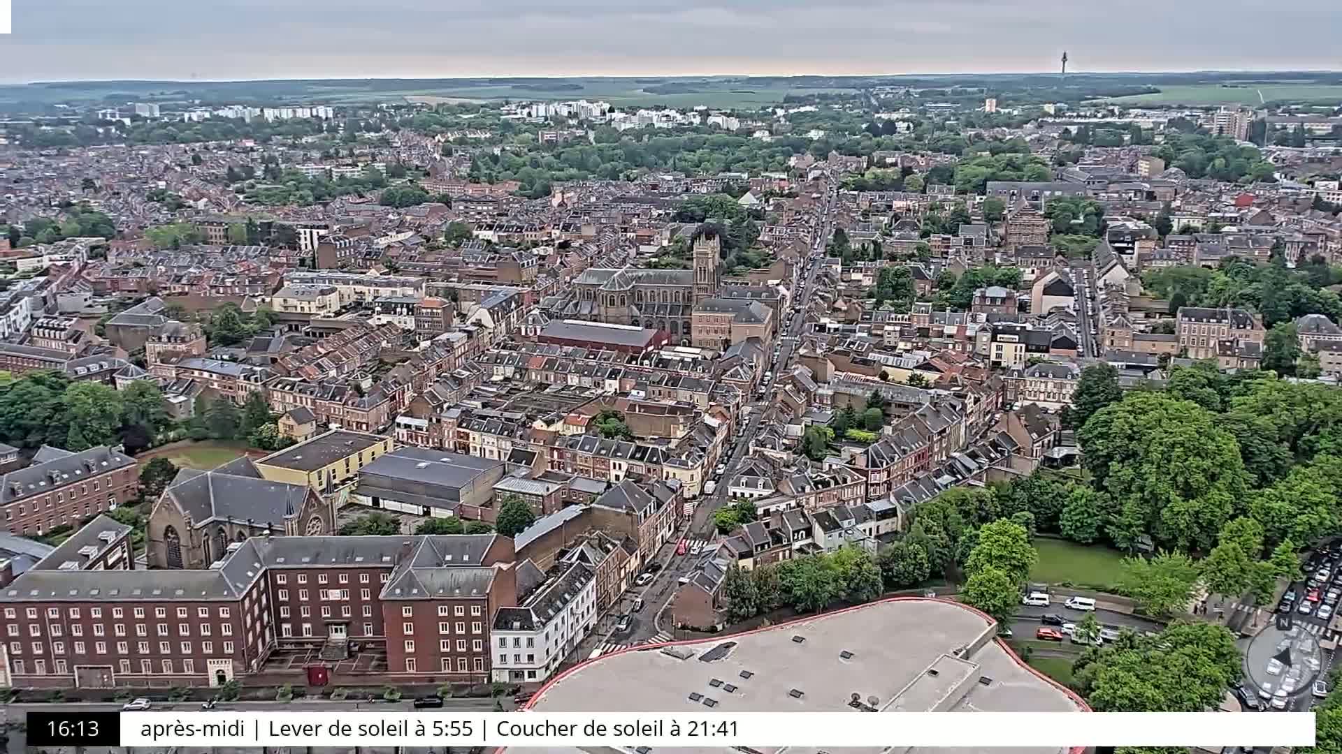 An aerial view of a densely populated city on an overcast day shows numerous brick buildings, green spaces, and roadways.