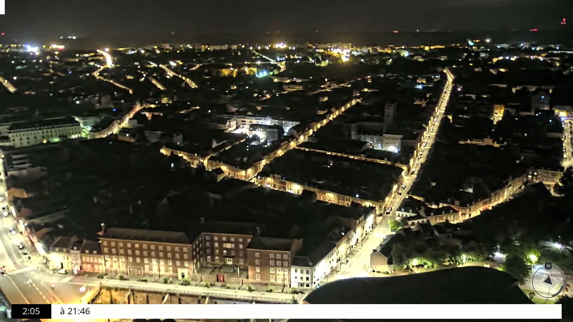 A nighttime aerial view shows a city with streets lined with illuminated buildings.