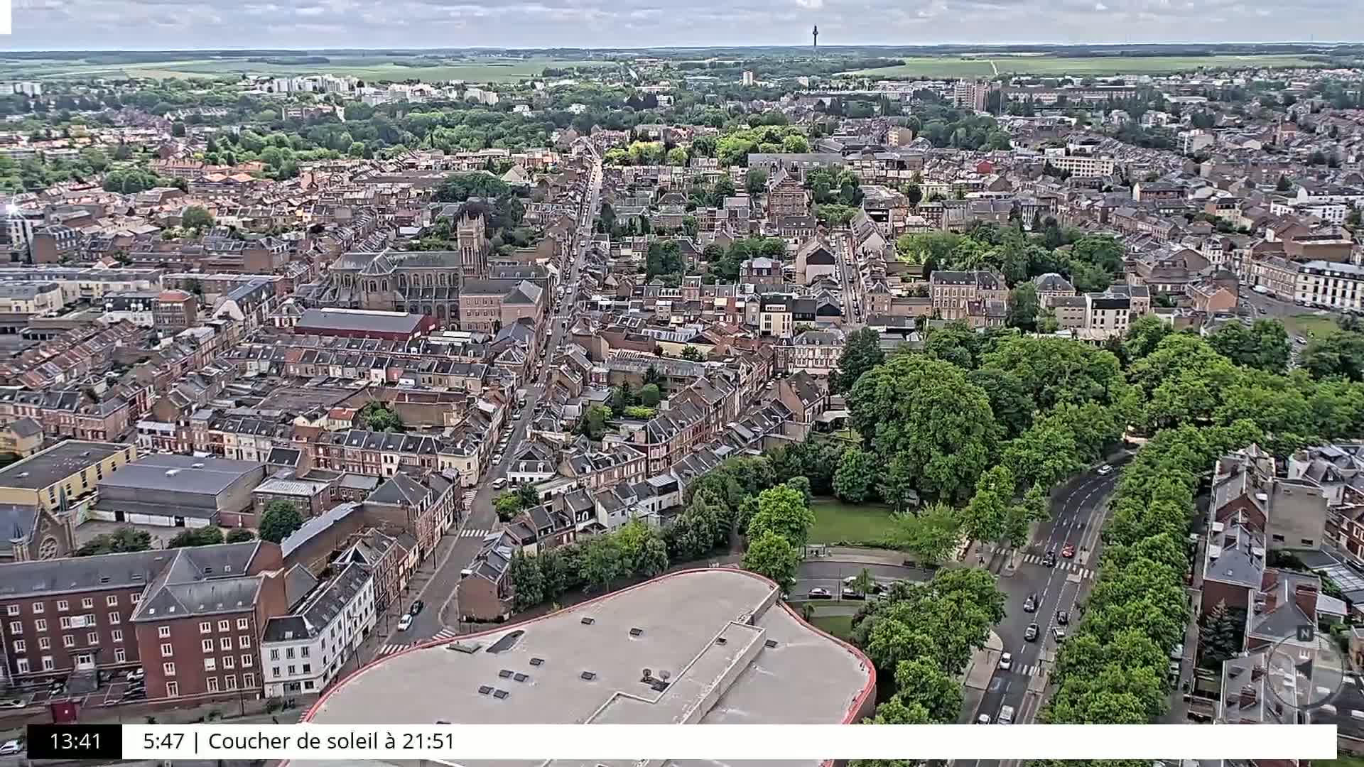 An aerial view of a densely packed town under an overcast sky, showing numerous buildings, green spaces, and roads.