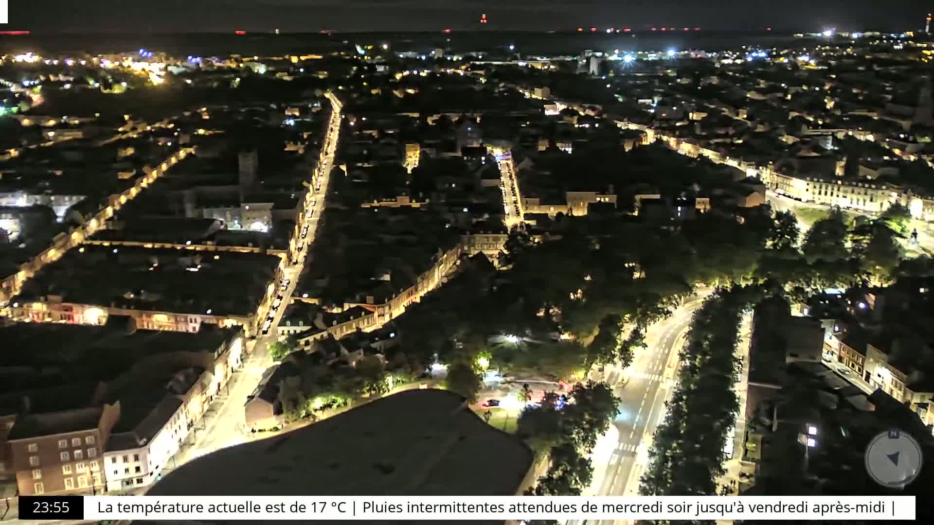 A nighttime aerial view of a city with brightly lit streets winding through buildings and green spaces.