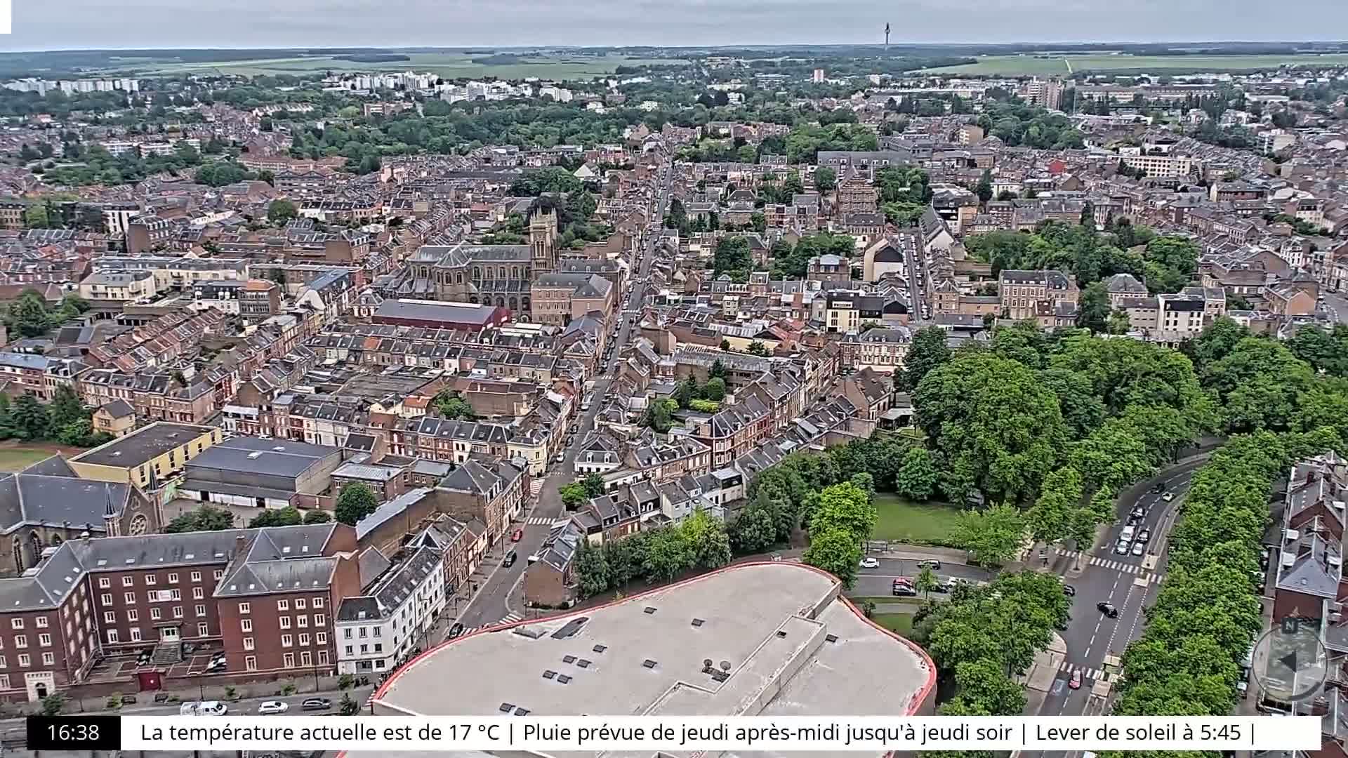 An aerial view shows a densely populated city with a mix of residential and commercial buildings under an overcast sky.