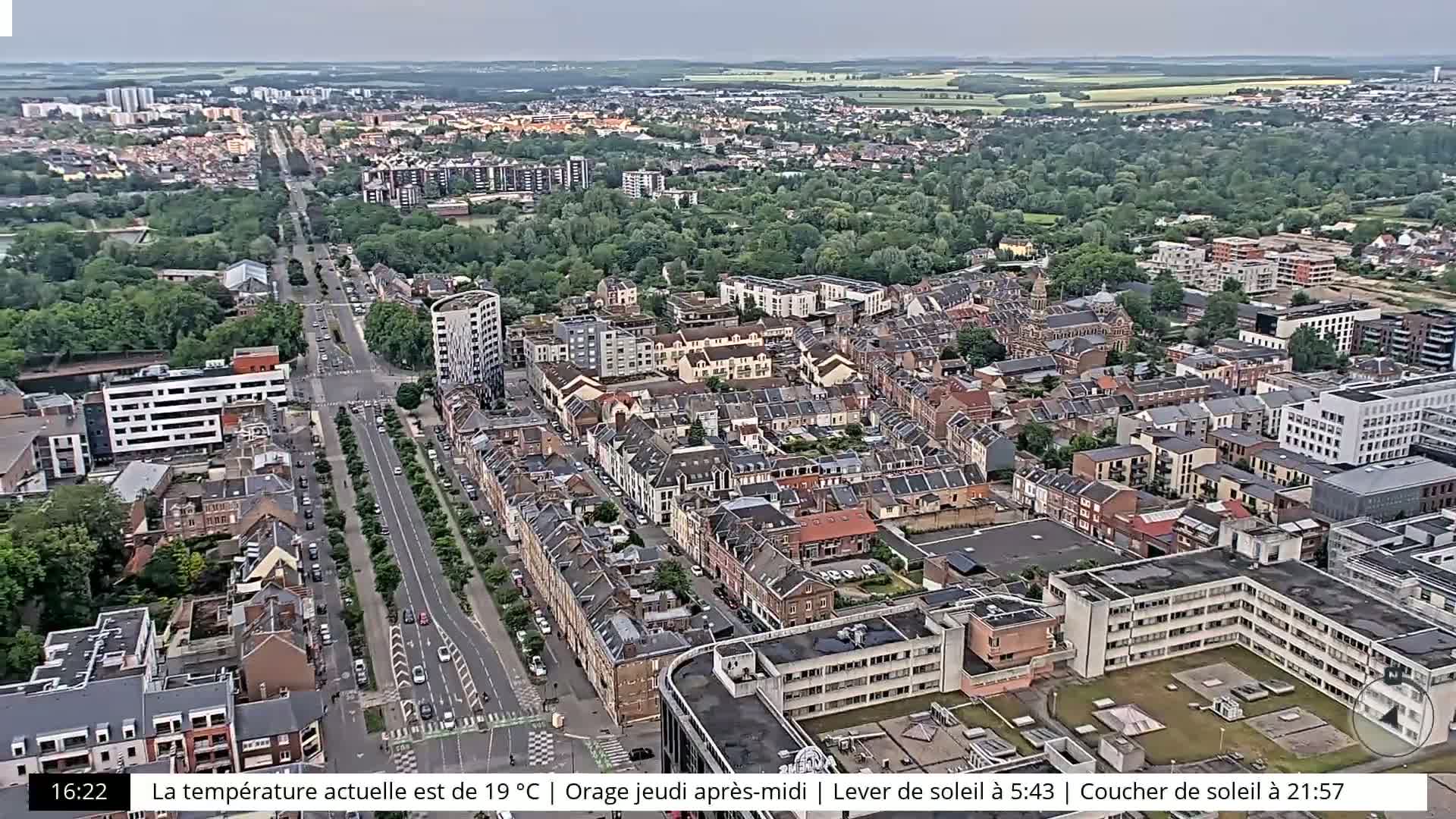 An aerial view of a city with many buildings and tree-lined streets under an overcast sky.