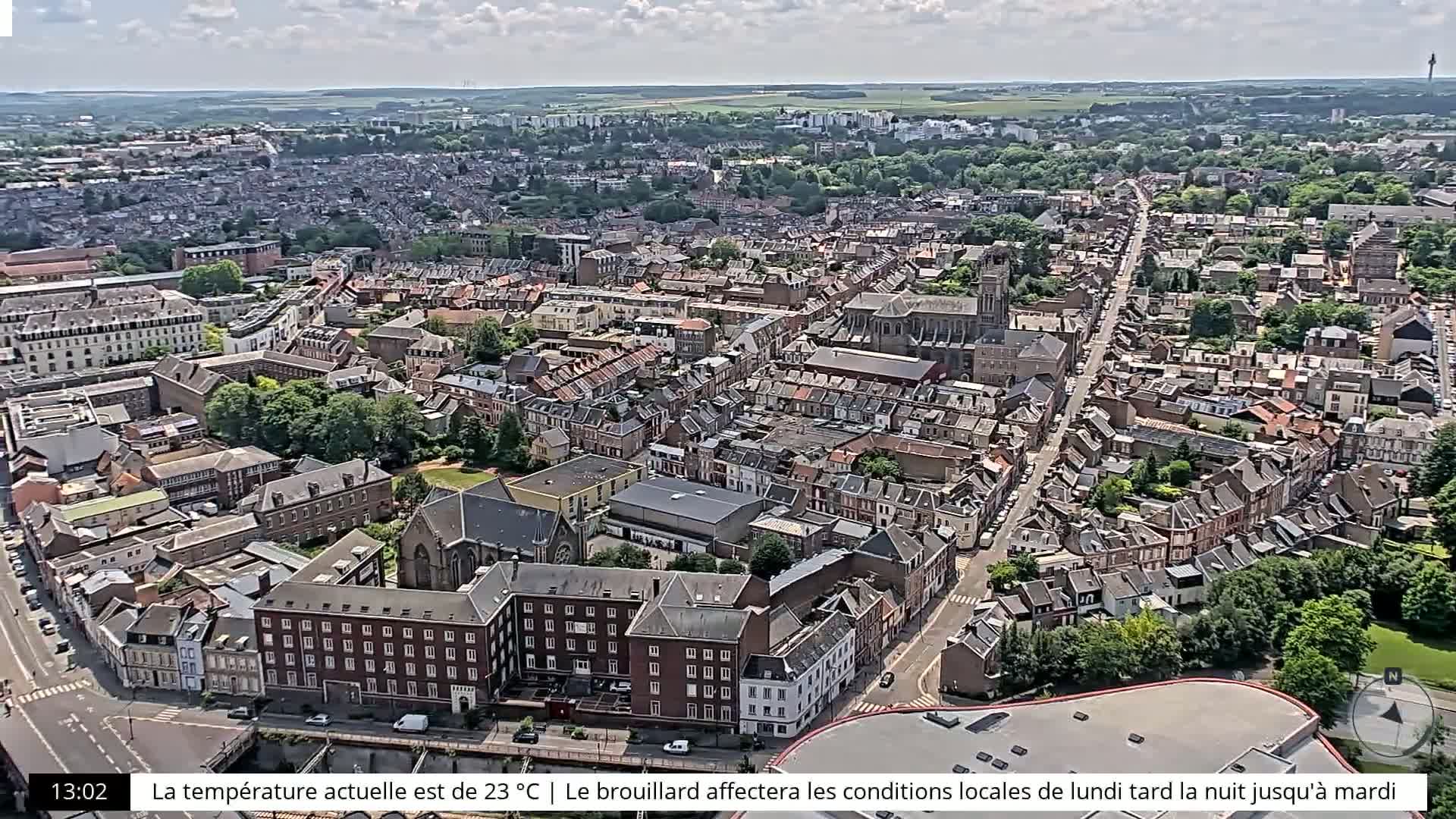 An aerial view shows a densely populated town with primarily brick buildings under partly cloudy skies.