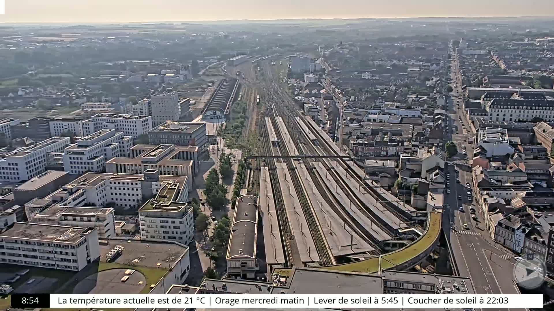 An aerial view of a city on a hazy day shows a large train station and numerous buildings surrounding it.