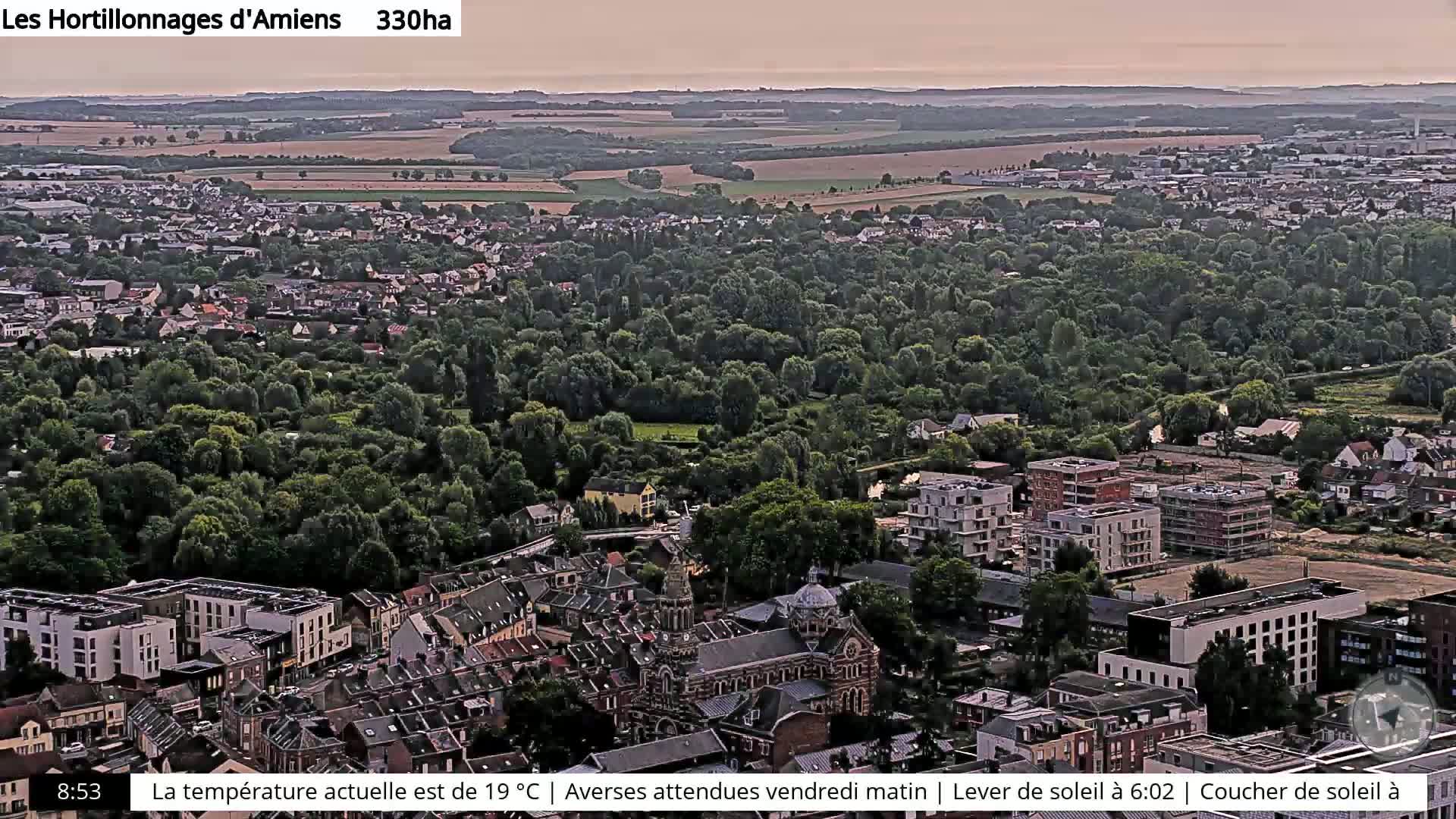 An aerial view of a town nestled among green trees and fields under a hazy sky.