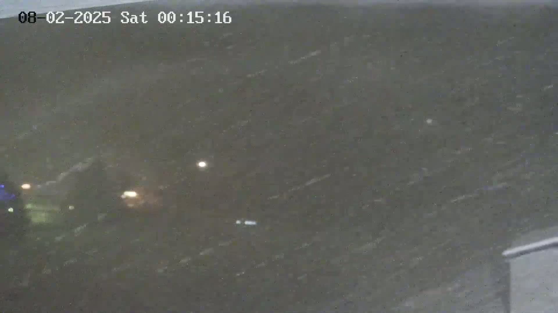 A nighttime, snowy scene shows blurry images of vehicles and lights on a dark road.